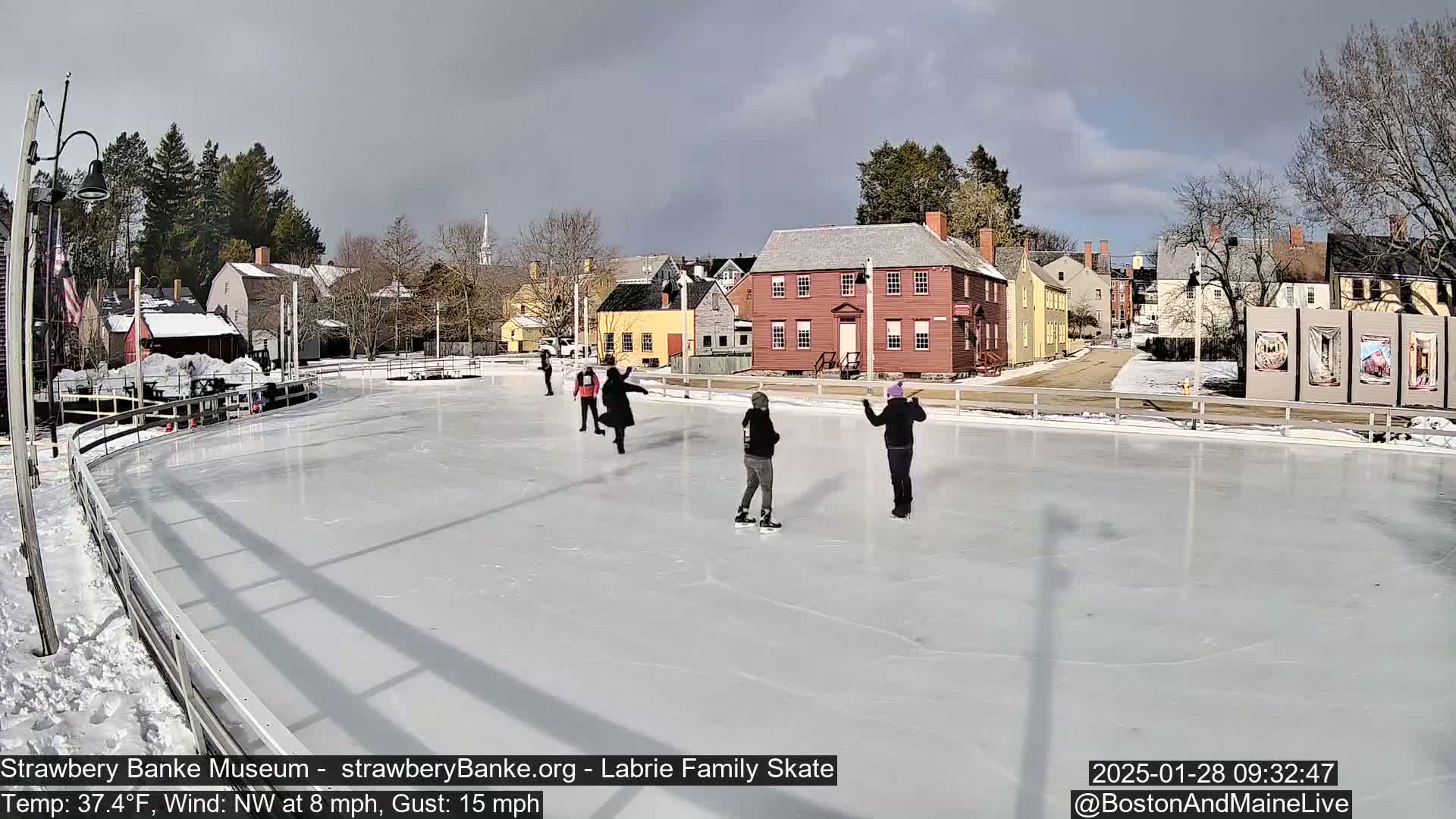 Several people ice skate on an outdoor rink in front of historic buildings on a partly cloudy day with a northwest wind.