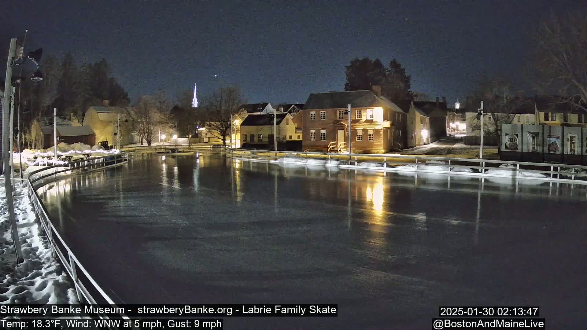 A nighttime view of an outdoor ice skating rink surrounded by illuminated historic buildings under a clear, starry sky.