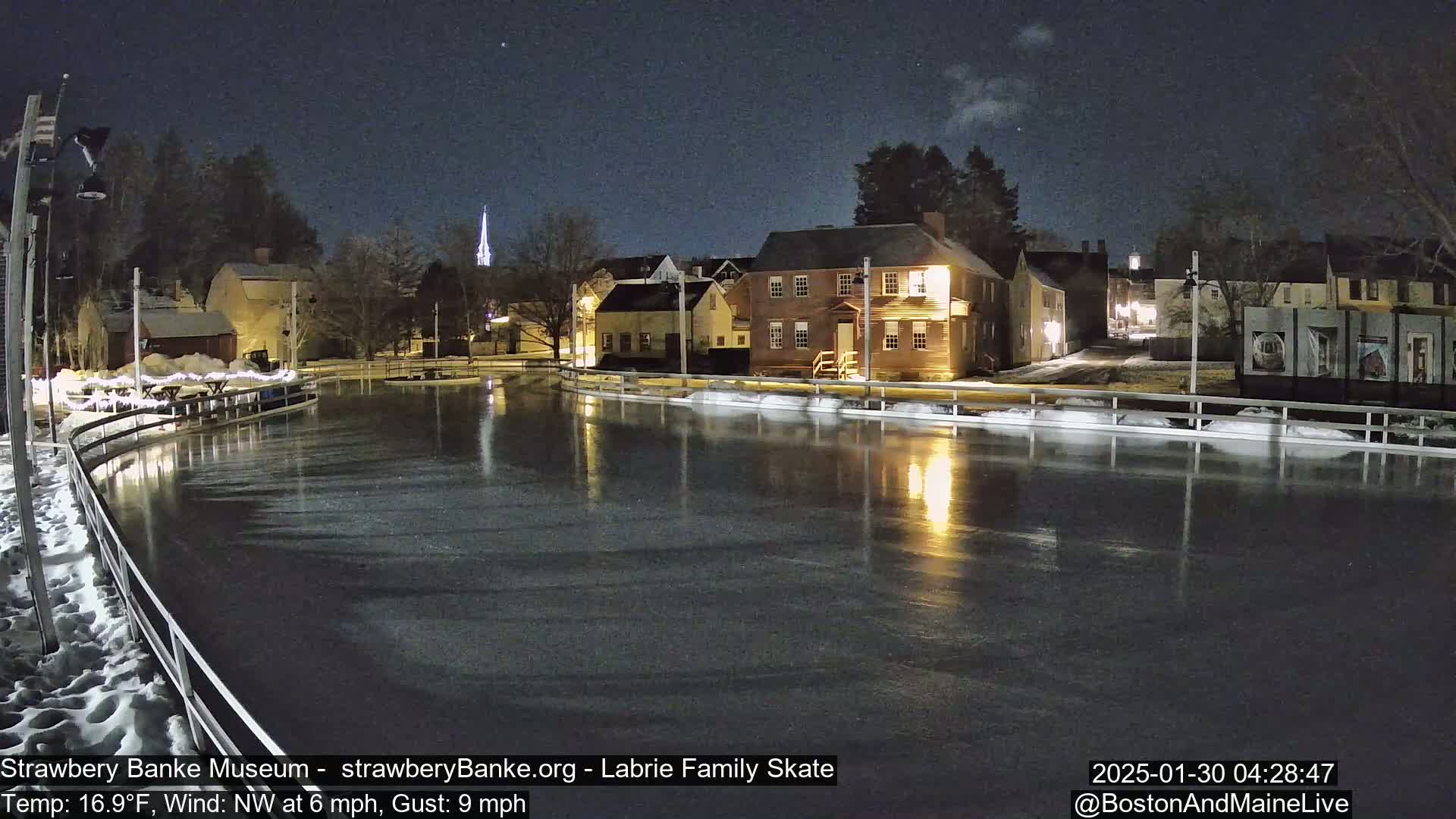A nighttime view of an ice skating rink reflecting the lights of nearby buildings under a clear, starry sky.