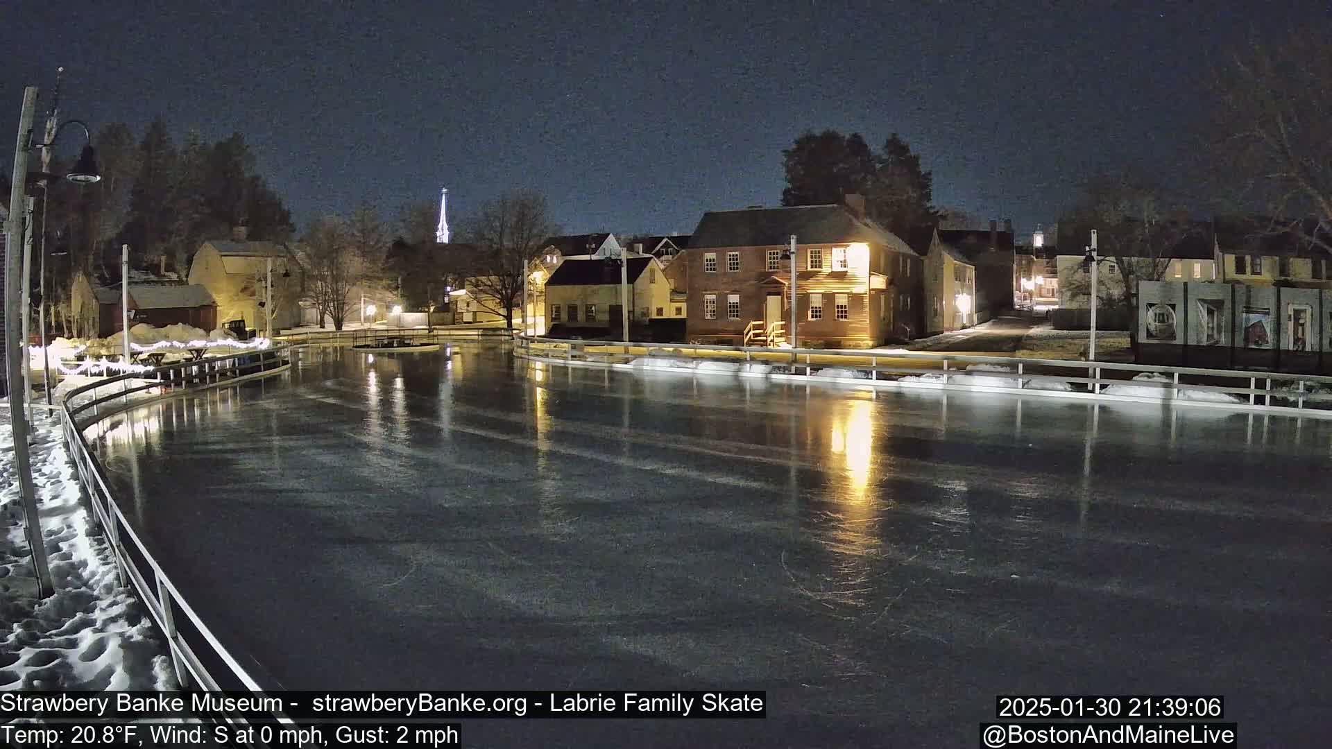 A nighttime view of an ice skating rink illuminated by nearby buildings, under a clear, dark sky.