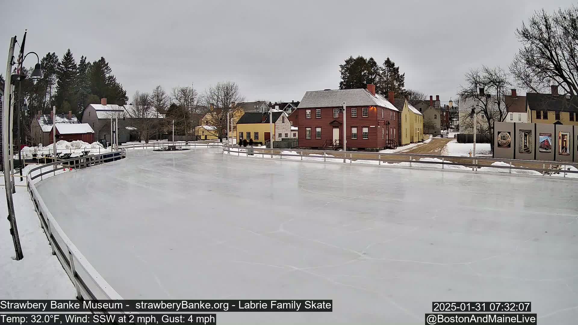 An outdoor ice skating rink, surrounded by historic-looking buildings under an overcast sky.
