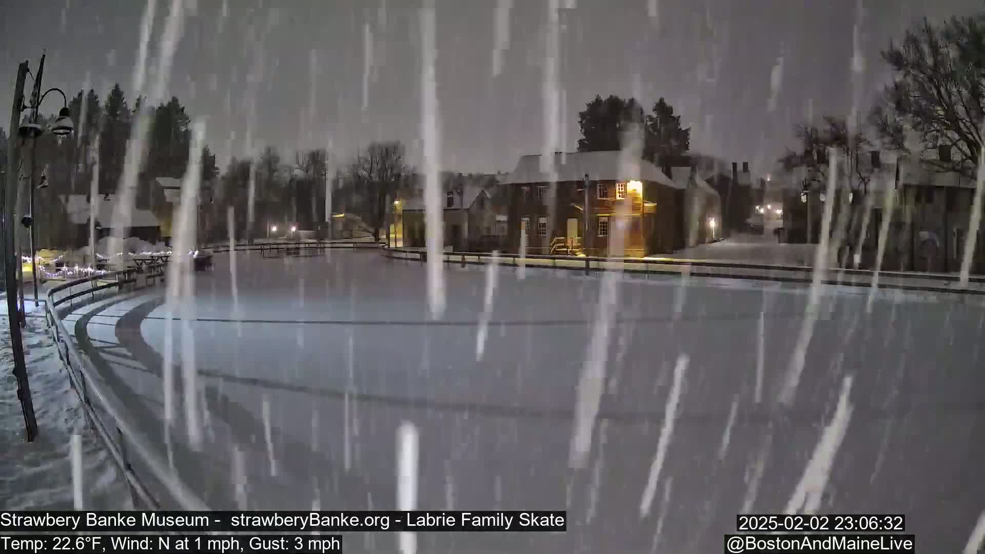 A snow-covered outdoor skating rink is seen at night under heavy snowfall.