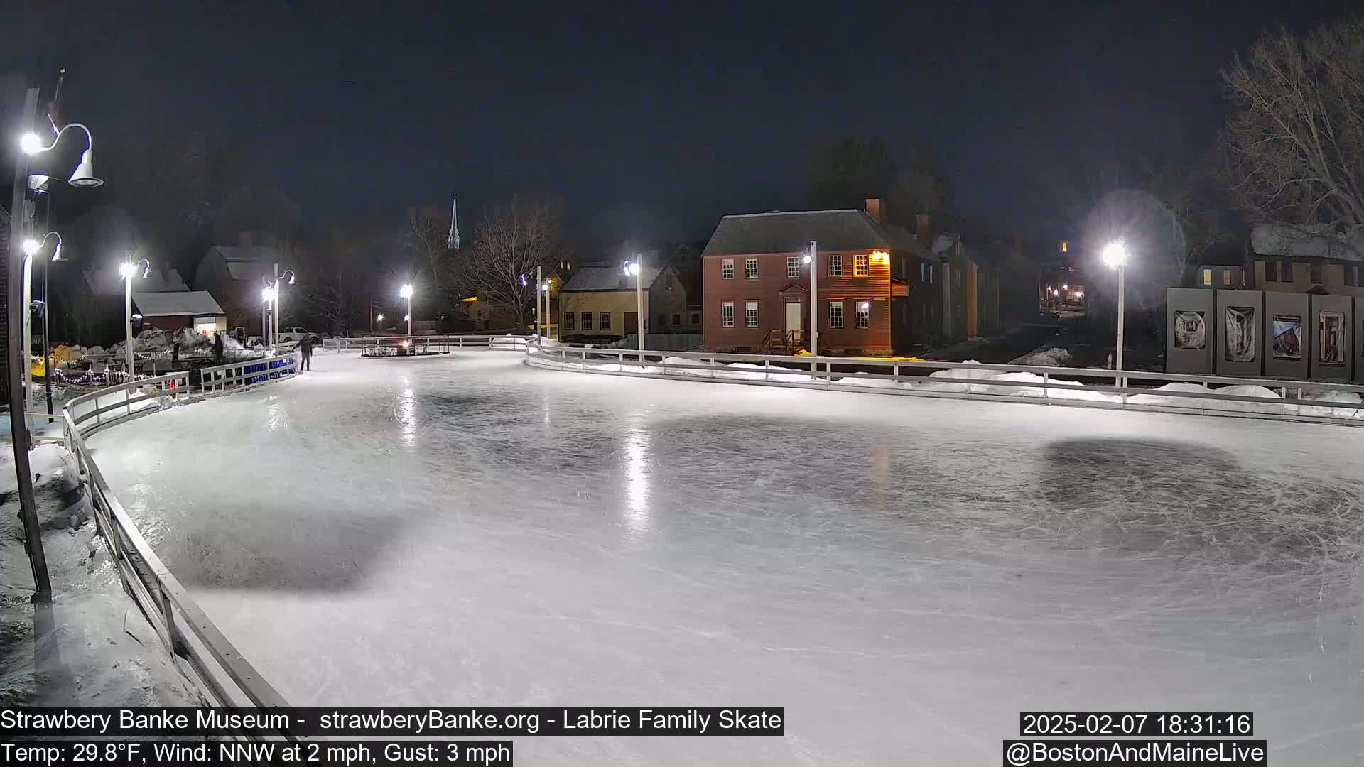 An outdoor ice skating rink at night, illuminated by lights, is surrounded by historic buildings under a clear, dark sky.