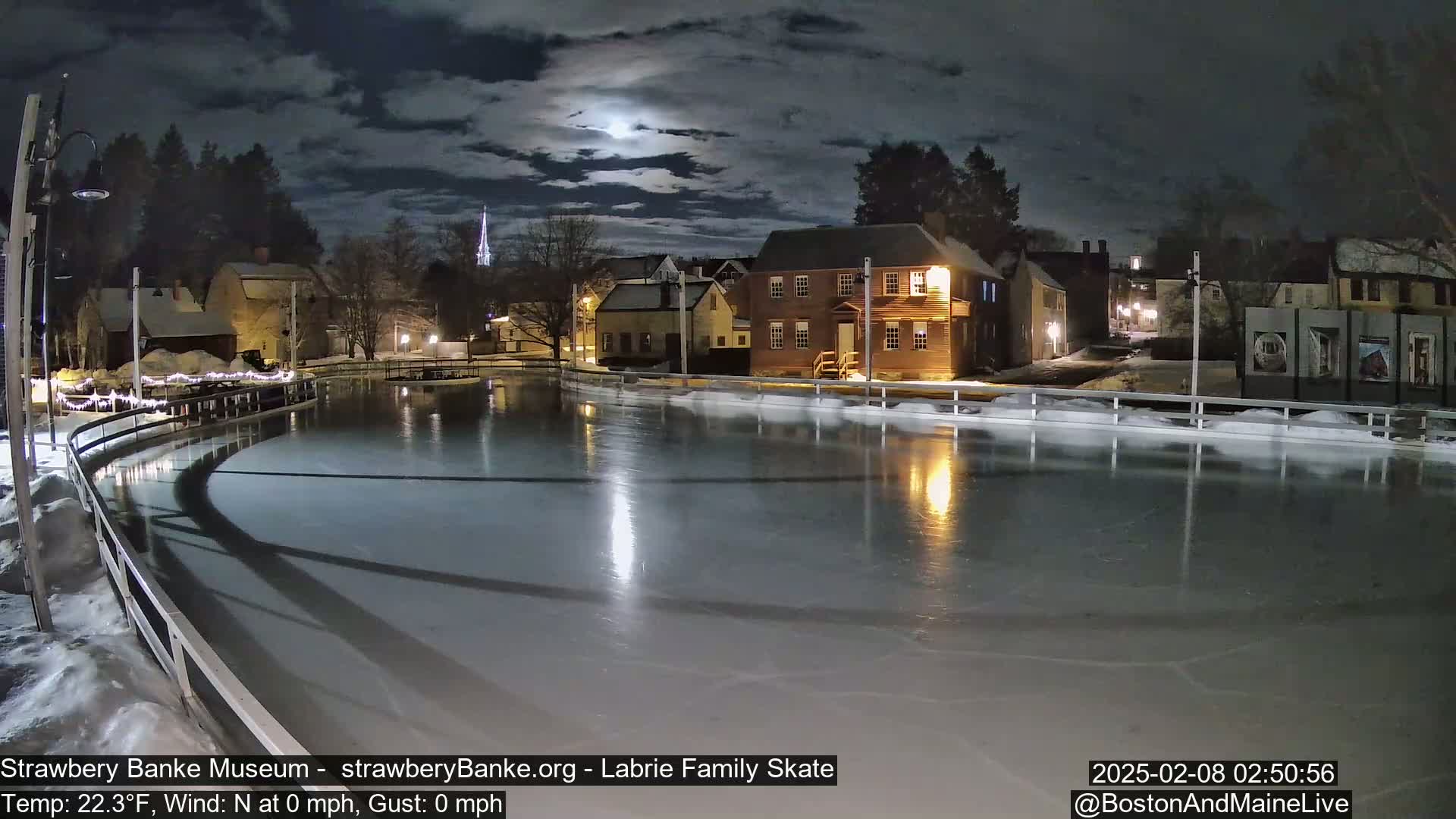 A moonlit night scene shows an outdoor ice skating rink next to historic buildings, under a partly cloudy sky.