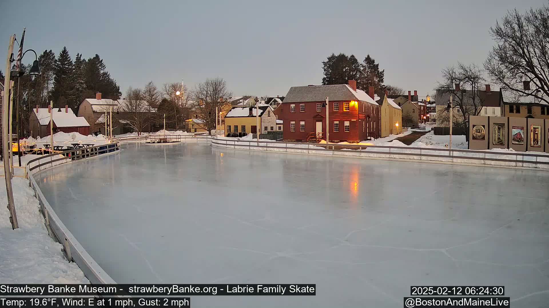 A frozen outdoor skating rink is situated in front of a row of historic buildings under a twilight sky.