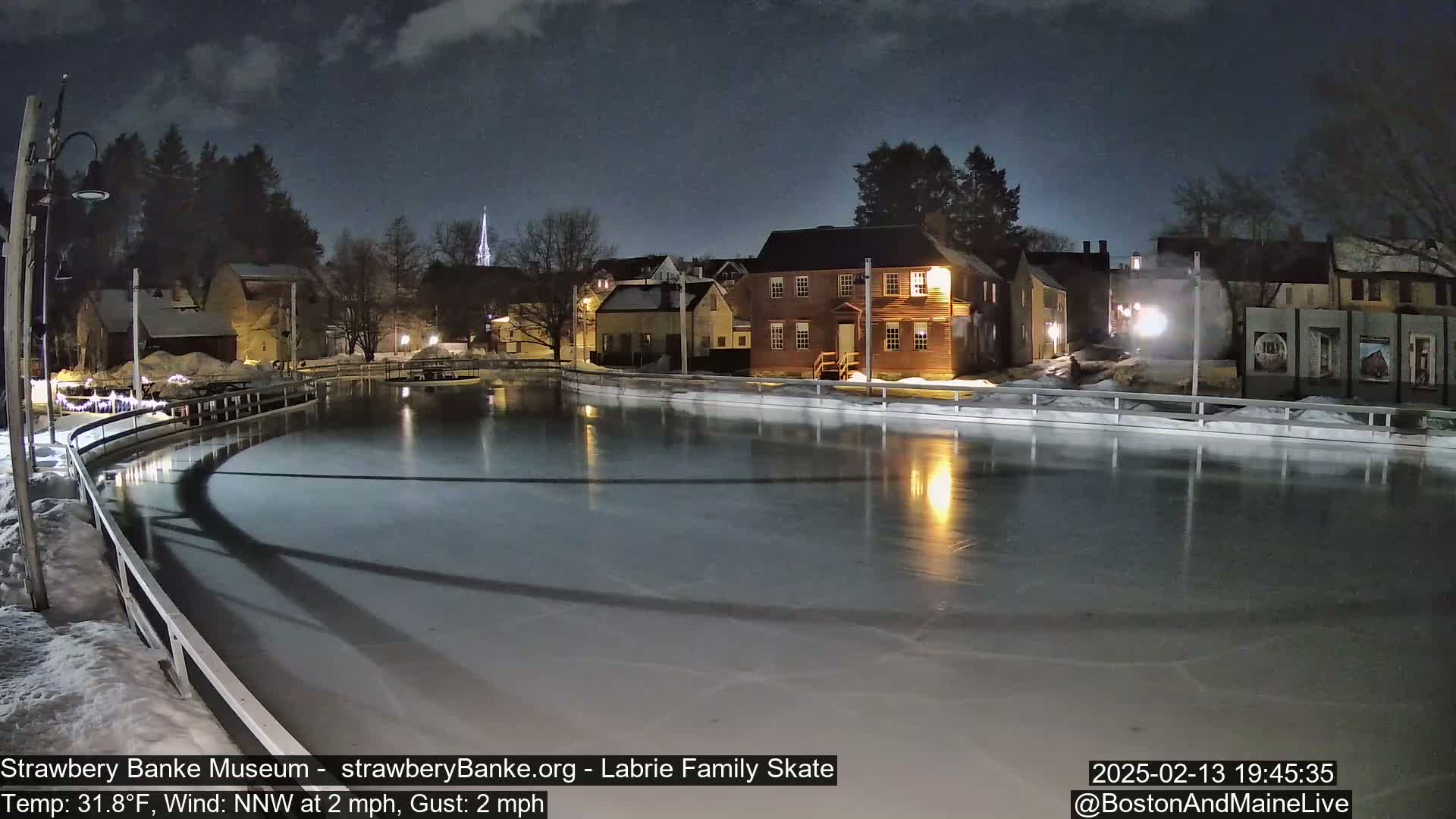 An outdoor ice skating rink at night, illuminated by lights, is surrounded by historic-looking buildings under a mostly clear, dark sky.