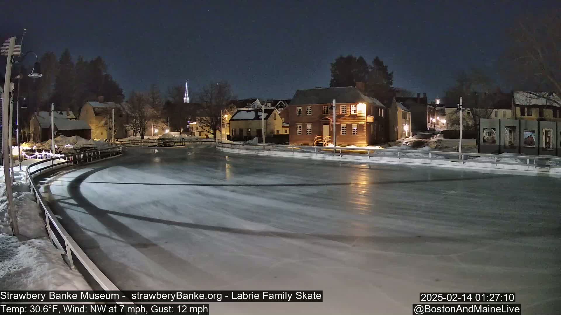 An outdoor ice skating rink at night, illuminated by lights from nearby buildings, under a clear night sky with a northwest wind.