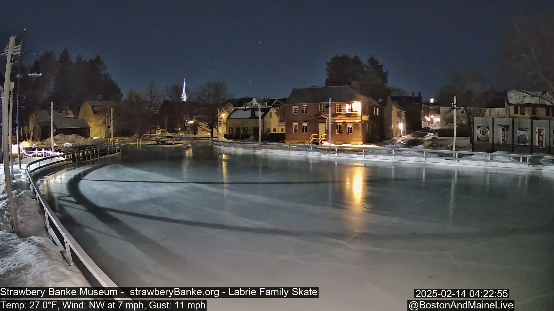 A nighttime view of an outdoor ice rink illuminated by lights, situated near historic buildings under a clear, starry sky.