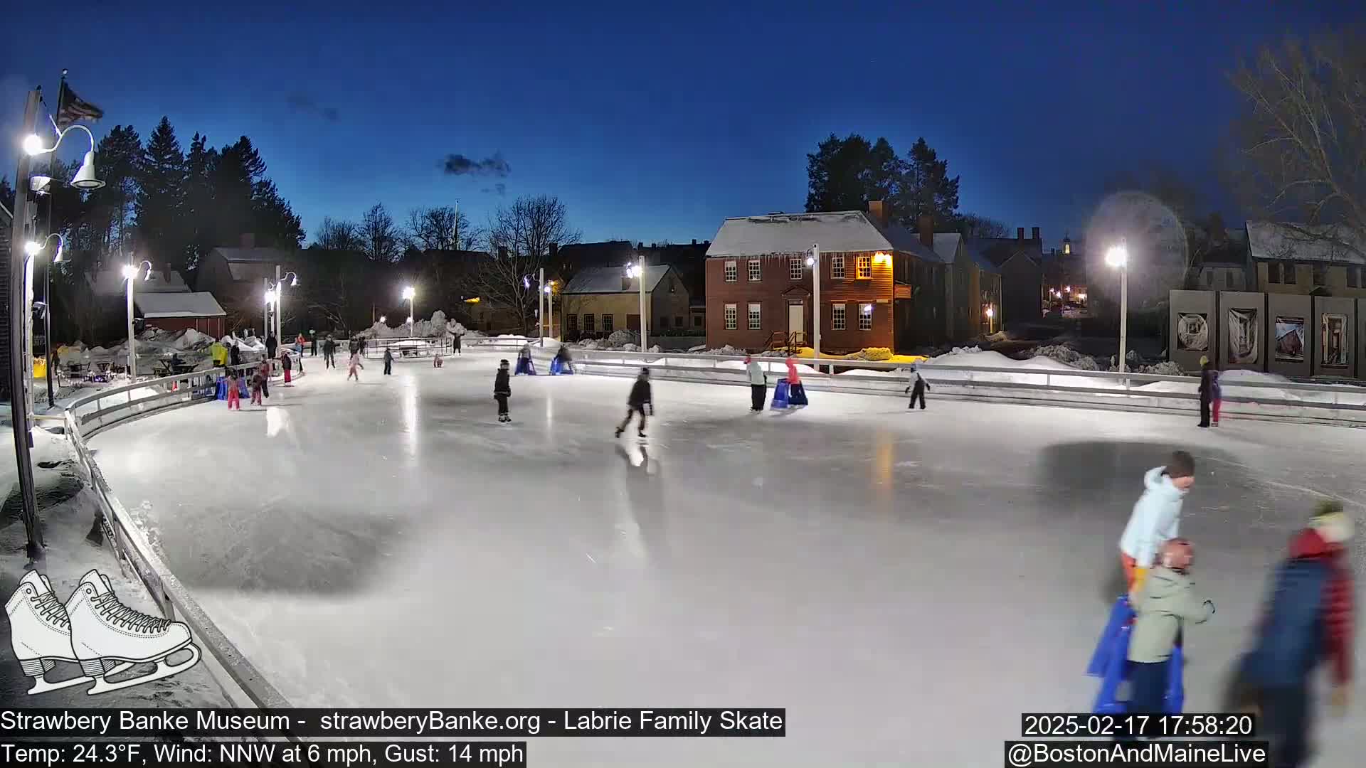 Many people ice skate on an outdoor rink at night under a clear, dark blue sky.