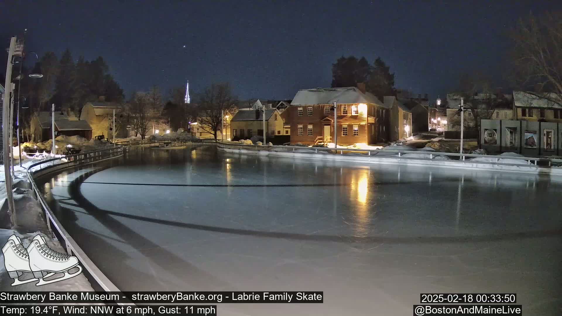 A nighttime view of an outdoor ice rink illuminated by lights, surrounded by historic-looking buildings under a clear, dark sky.