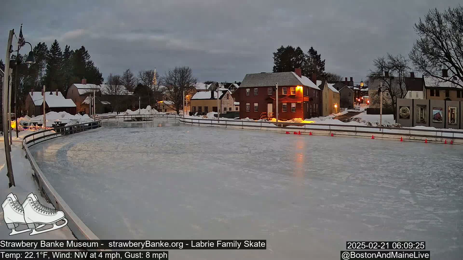 A frozen outdoor skating rink, surrounded by snow-covered historic buildings under a twilight sky with a northwest wind.