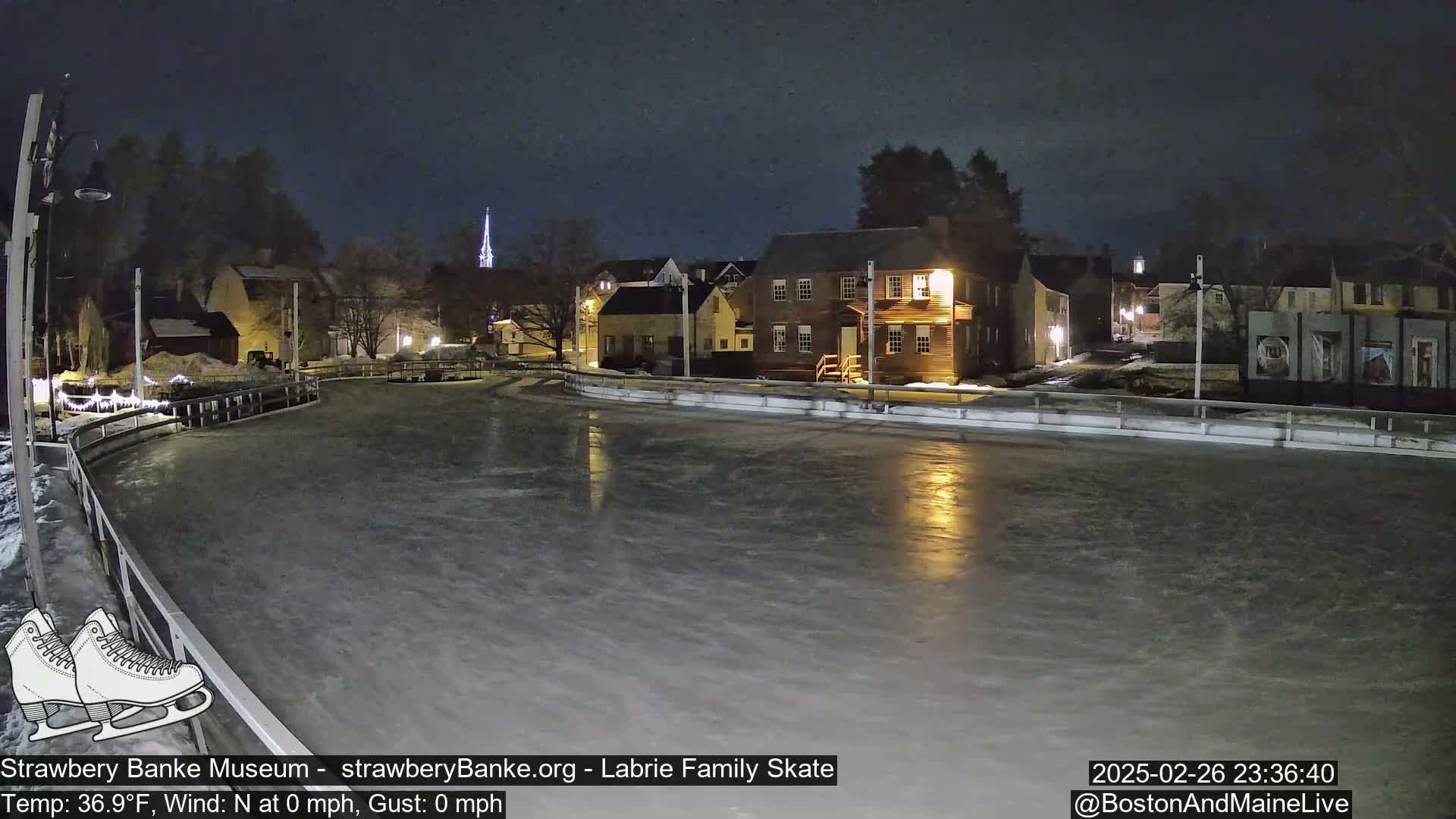 An outdoor ice rink at night, illuminated by nearby buildings, is mostly empty under a dark sky.