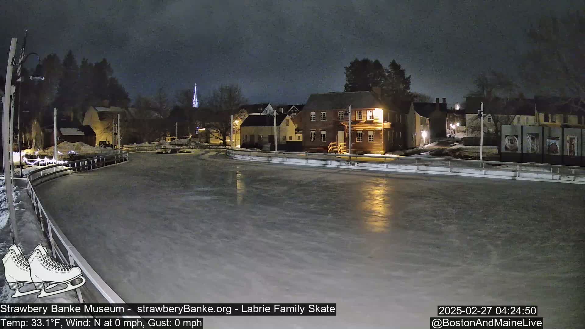 An outdoor ice skating rink at night, illuminated by nearby buildings, under a dark sky.