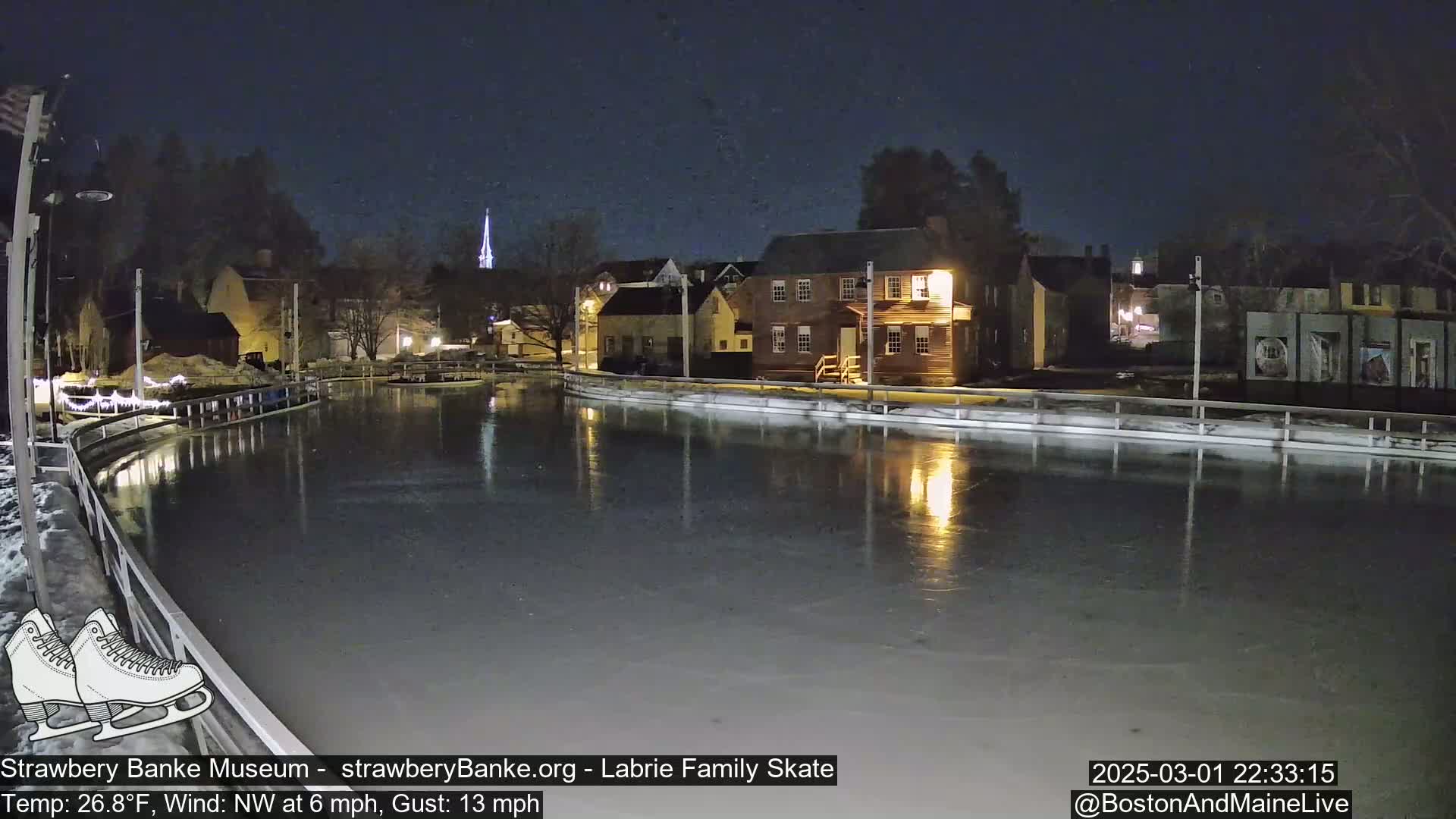 An outdoor ice skating rink at night, illuminated by lights reflecting on the ice, is surrounded by buildings under a dark, clear sky.
