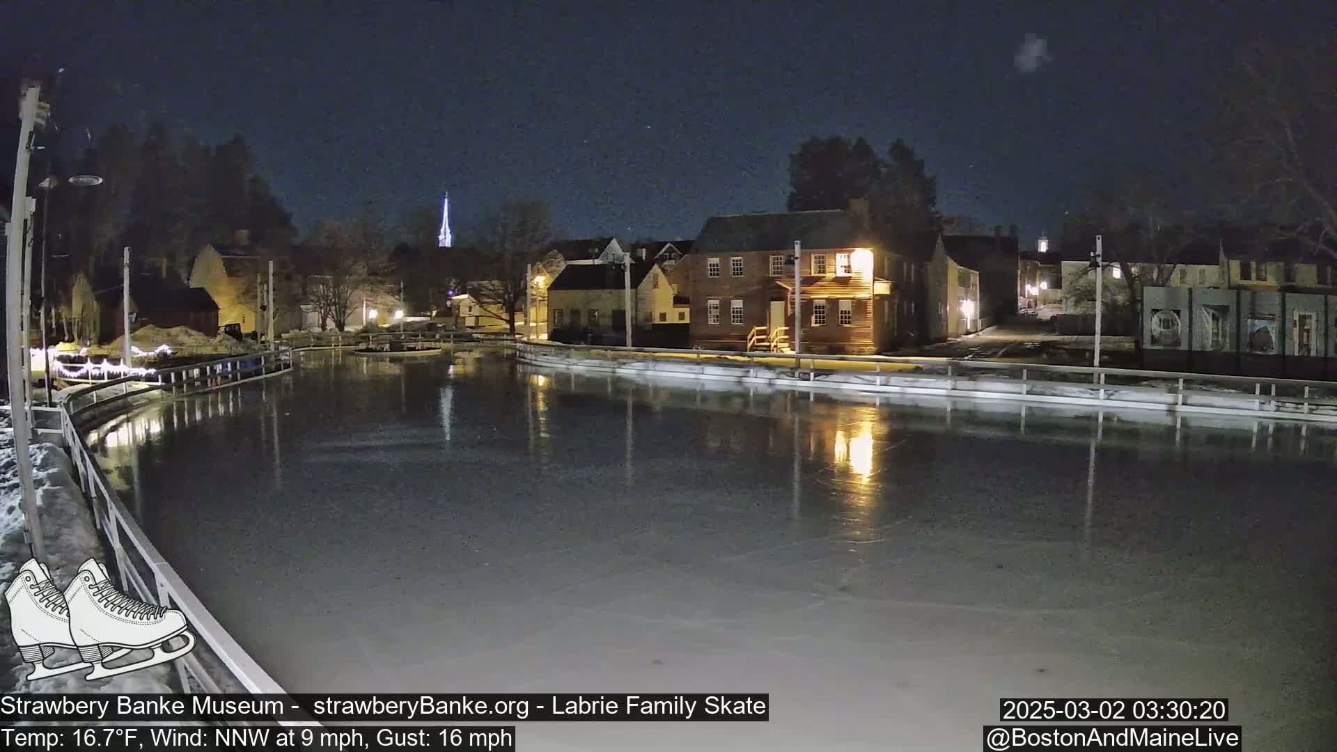 A nighttime view of an outdoor ice skating rink, illuminated by building lights, with a wind of 9 mph and gusts up to 16 mph, and a temperature of 16.7°F.