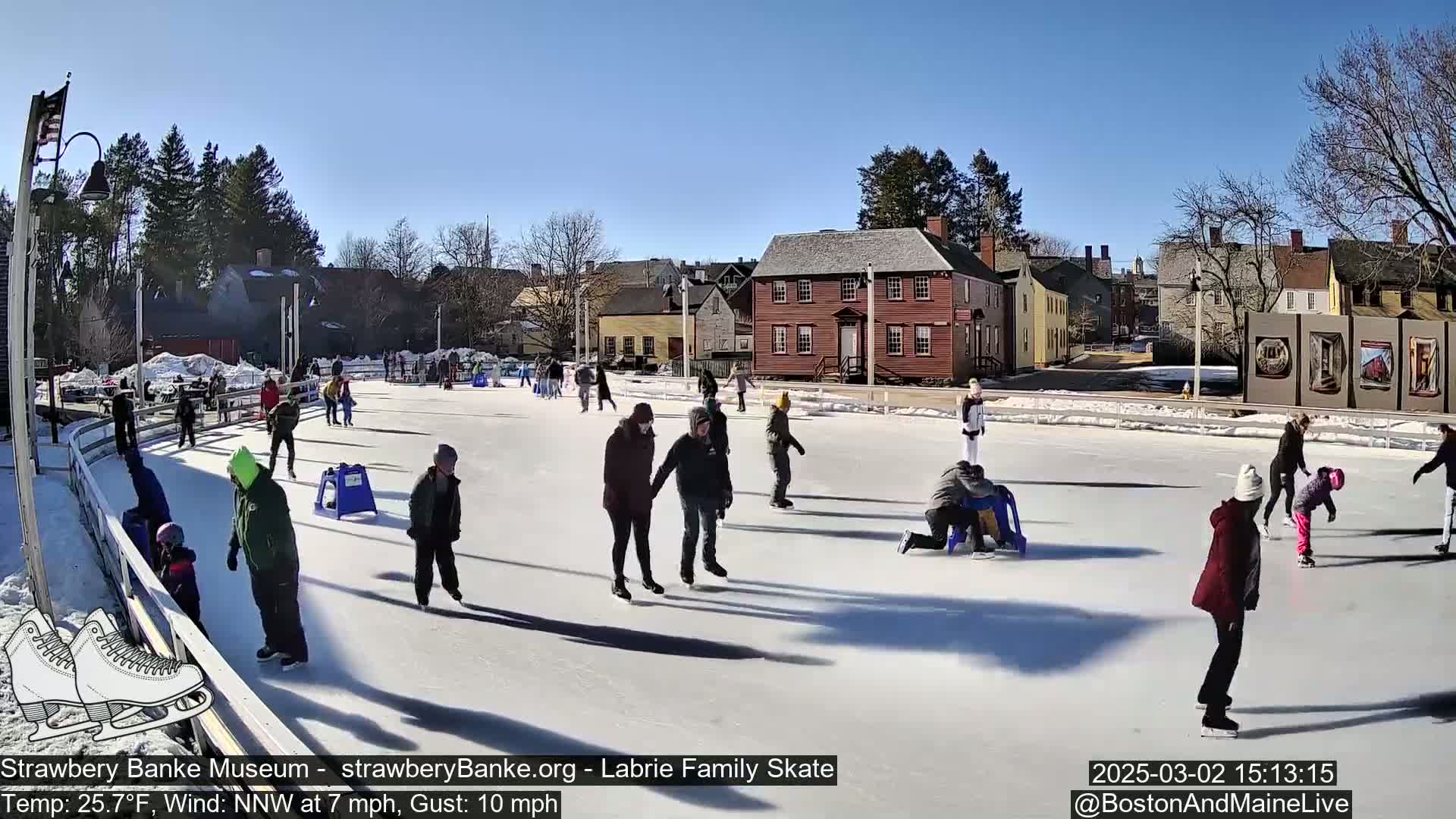 Many people ice skate on an outdoor rink on a sunny day with a temperature of 25.7°F, a north-northwest wind of 7 mph, and gusts up to 10 mph.