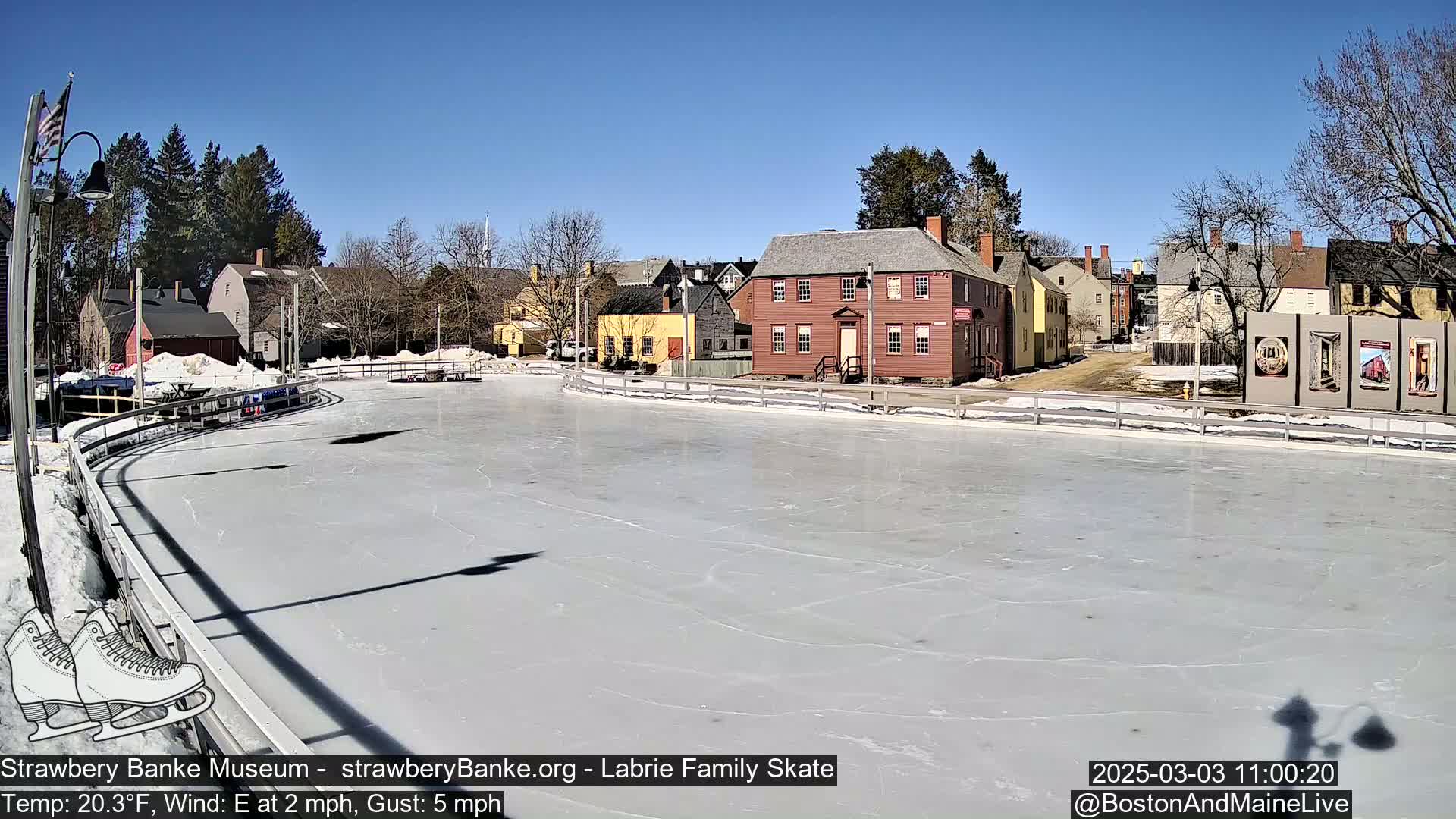 An outdoor ice skating rink, surrounded by historic buildings on a sunny day with an east wind of 2 mph and gusts up to 5 mph, and a temperature of 20.3°F.