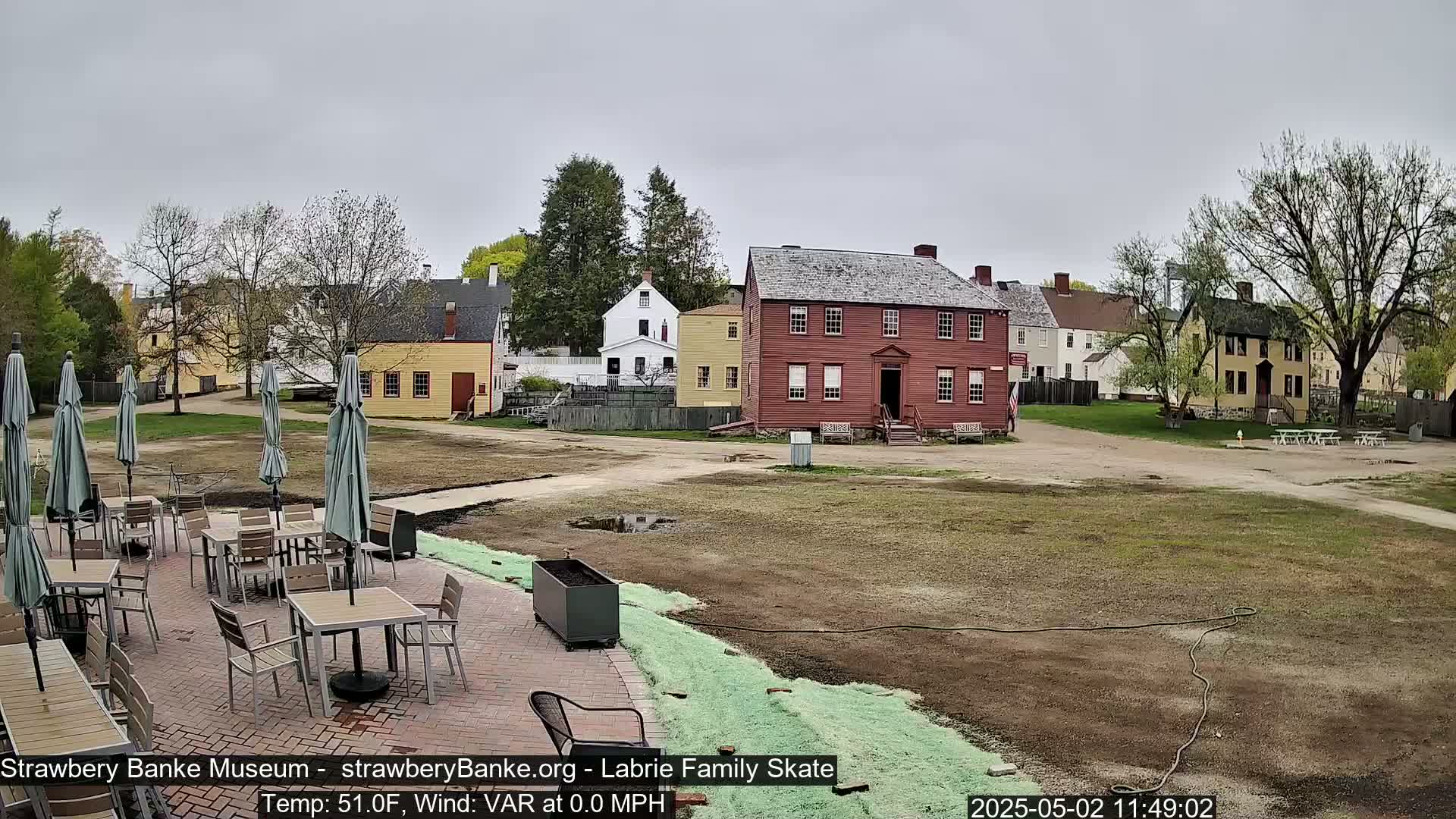A patio with tables and umbrellas sits in front of several historic-looking buildings on a mostly overcast day.