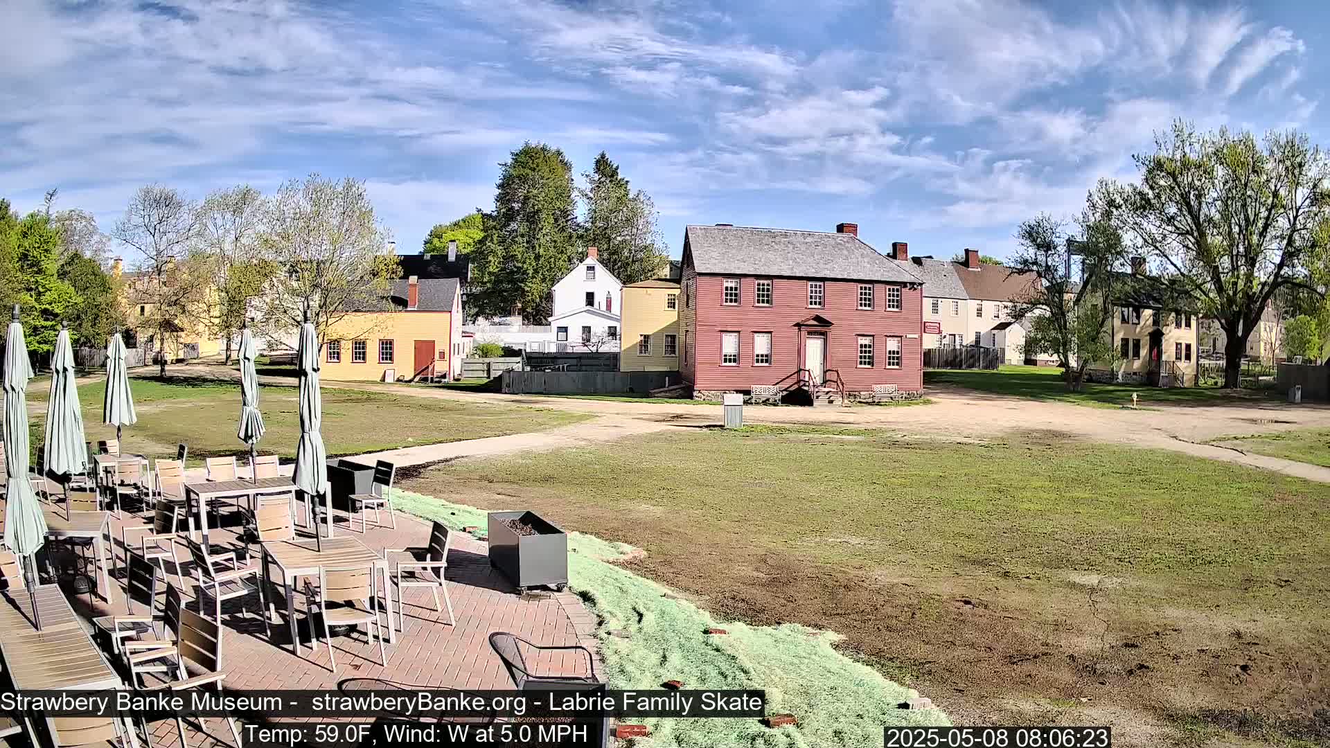 A sunny outdoor scene shows several colonial-era buildings and a patio area with tables and umbrellas.