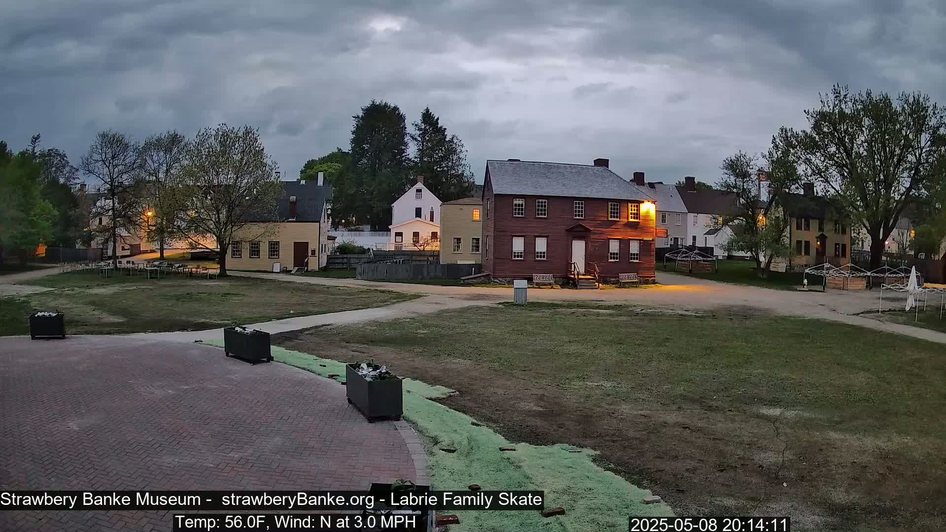 Several historical-looking buildings are situated on a grassy area under a cloudy, twilight sky.