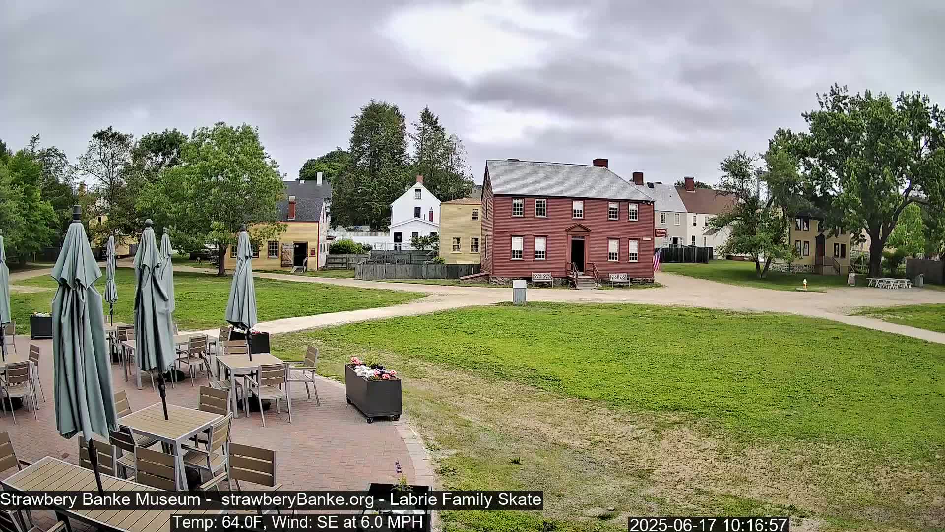 A courtyard with several tables and umbrellas under overcast skies, overlooks a collection of historic buildings.