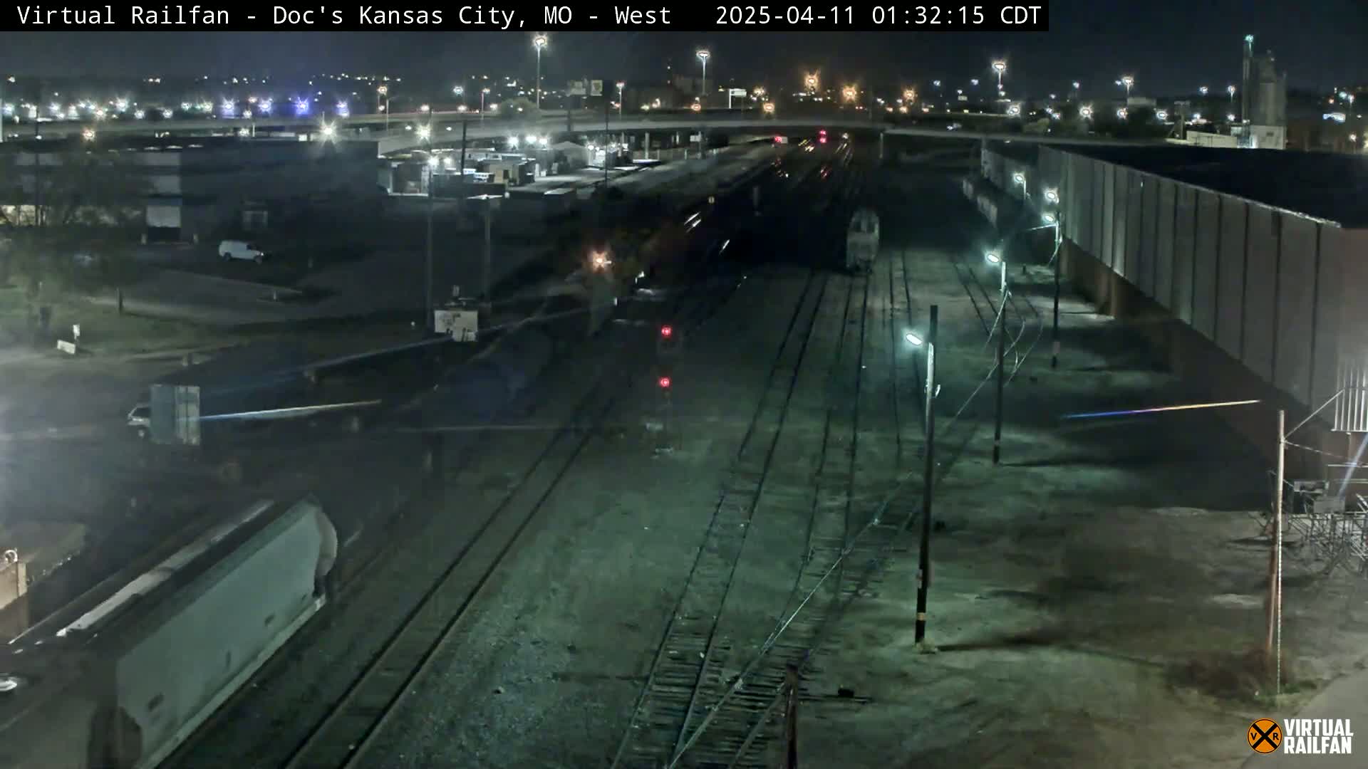 A nighttime view of a railway yard with trains and railcars, under clear skies.
