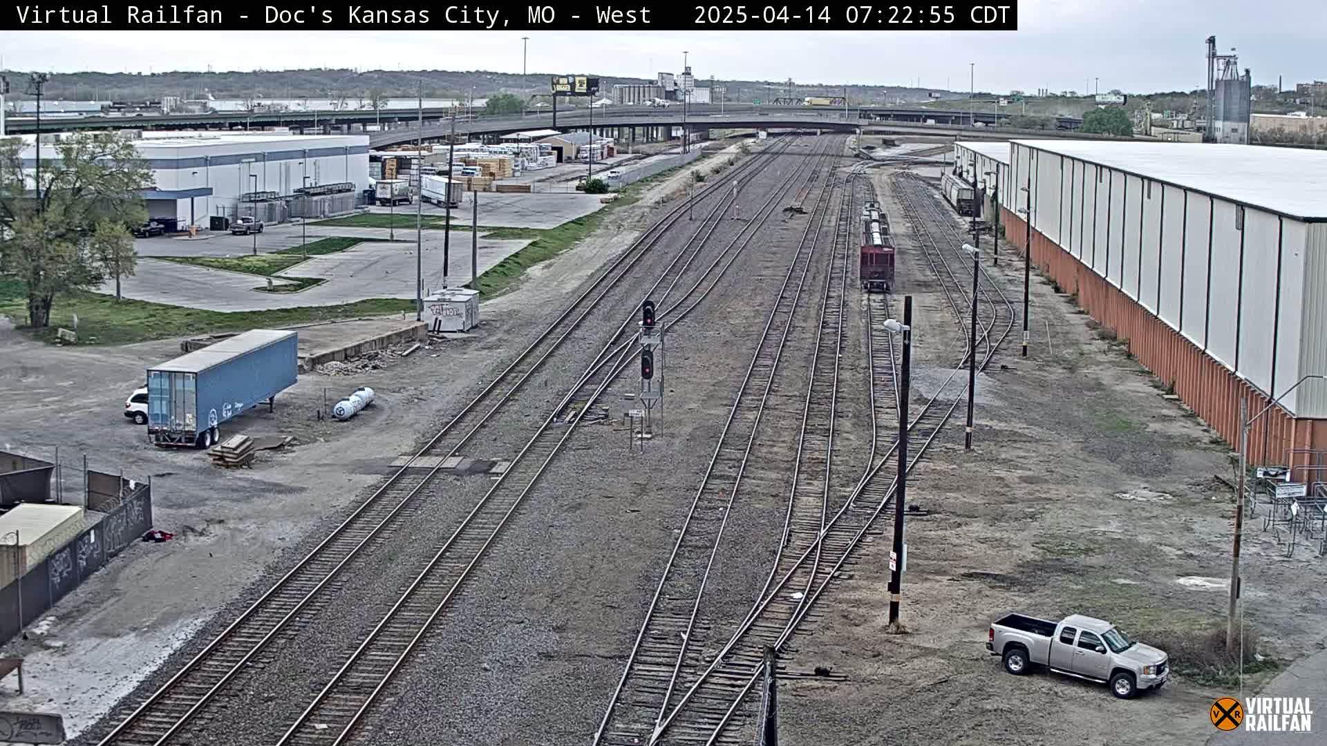 A high-angle view of a railroad yard with several train cars and trucks, surrounded by industrial buildings on an overcast day.