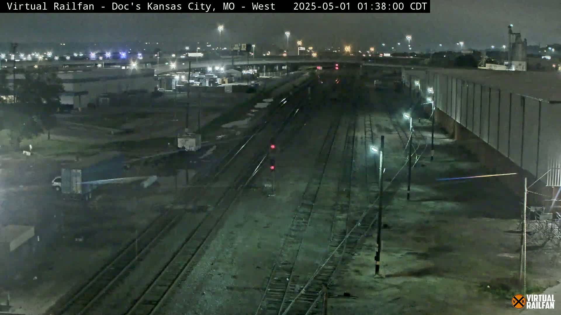 A nighttime view of railroad tracks and industrial buildings under a dark sky.
