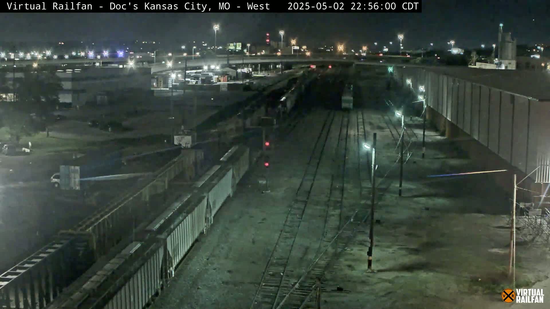 A nighttime, aerial view shows a train of boxcars in a rail yard under a clear sky.