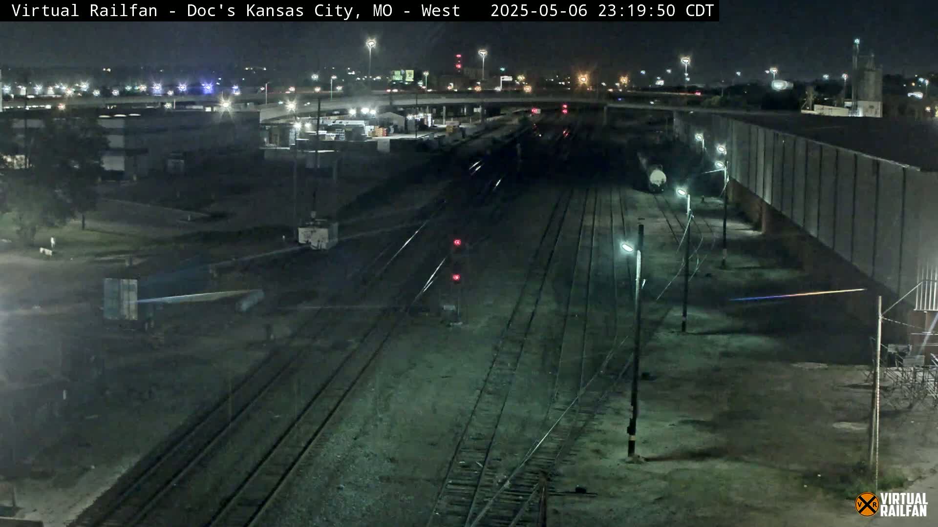 A nighttime view of a railroad yard with multiple train tracks, some buildings, and several lights illuminating the scene.