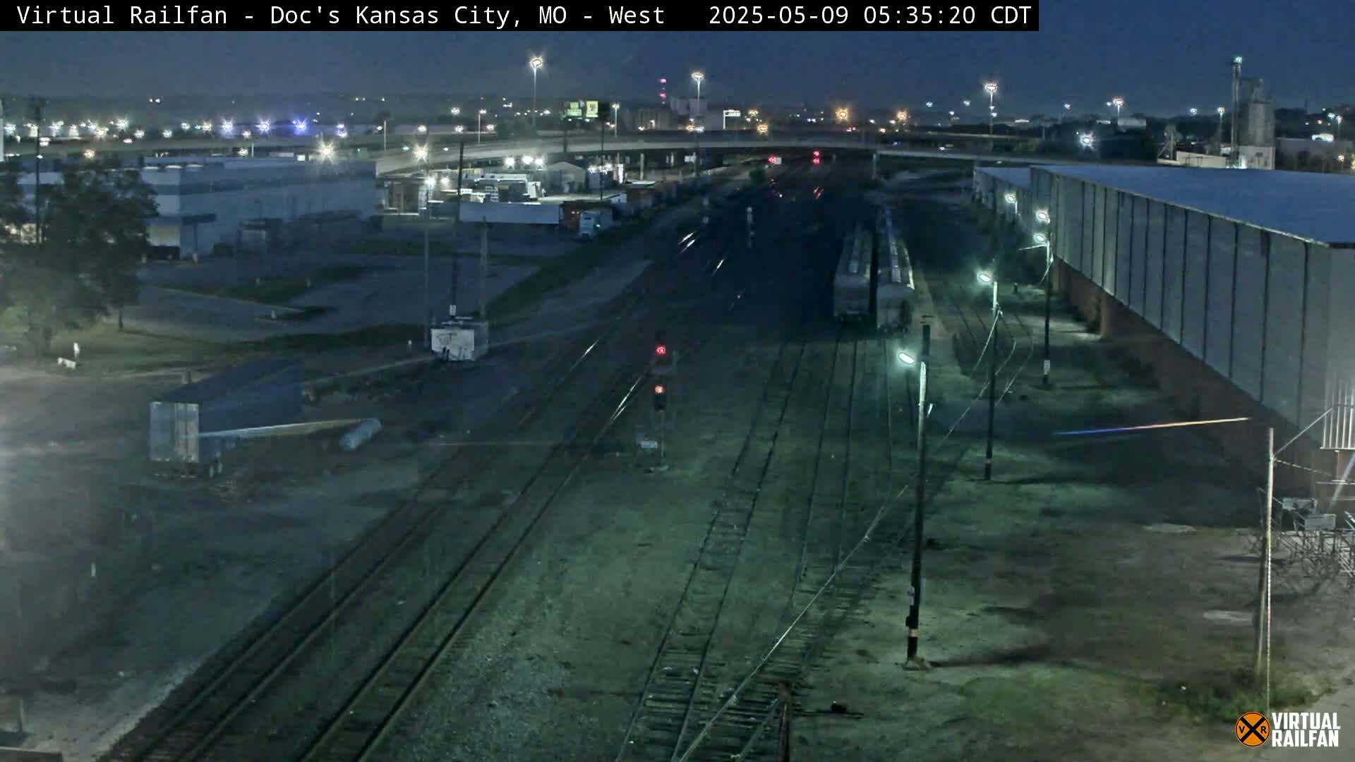 A nighttime view of railroad tracks and industrial buildings under a dark sky.