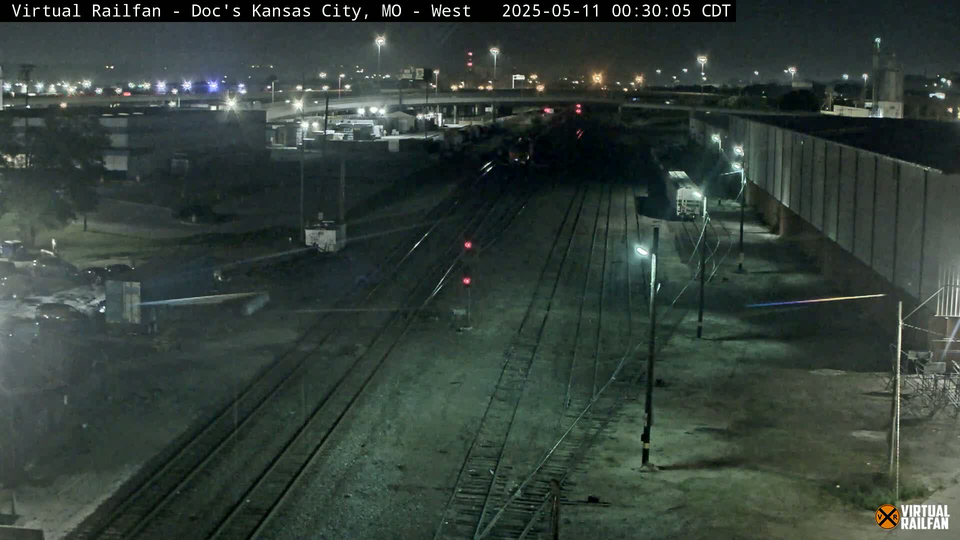 A nighttime view of train tracks and industrial buildings under a clear sky.