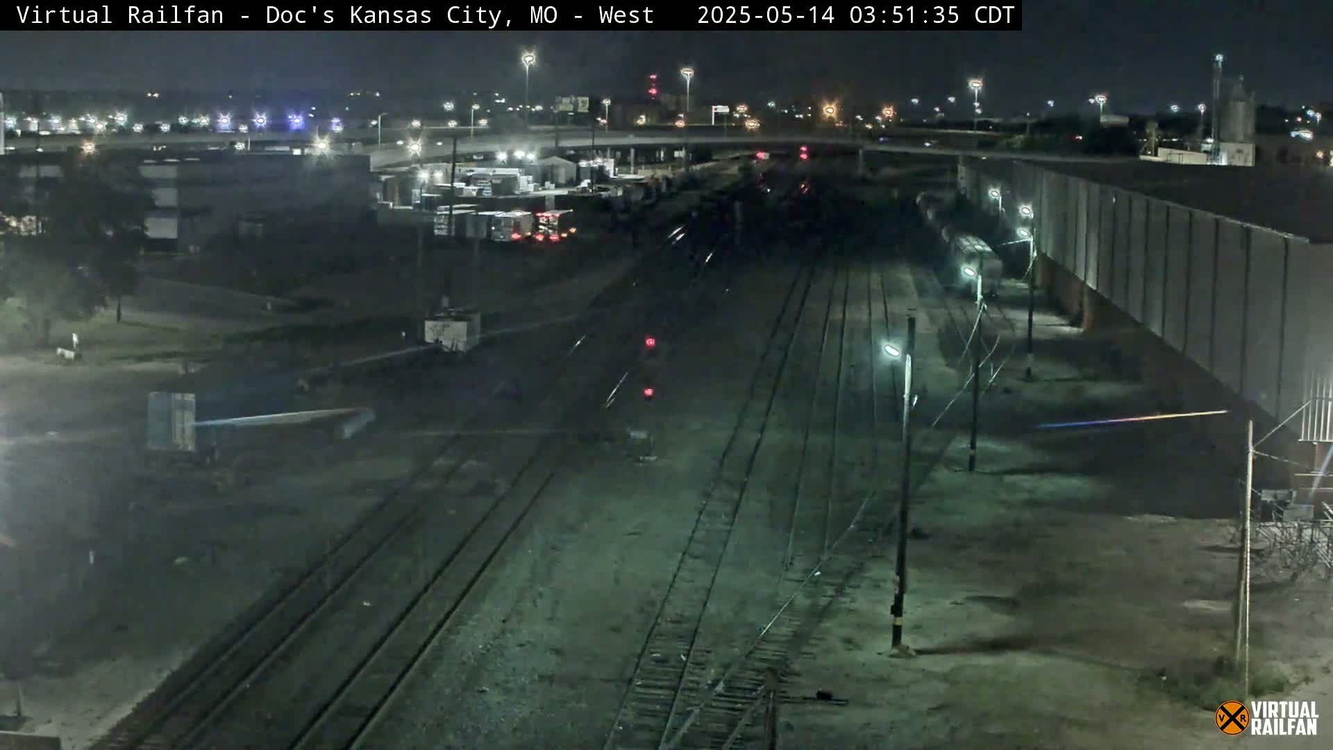 A nighttime view of railroad tracks and industrial buildings under a clear sky.