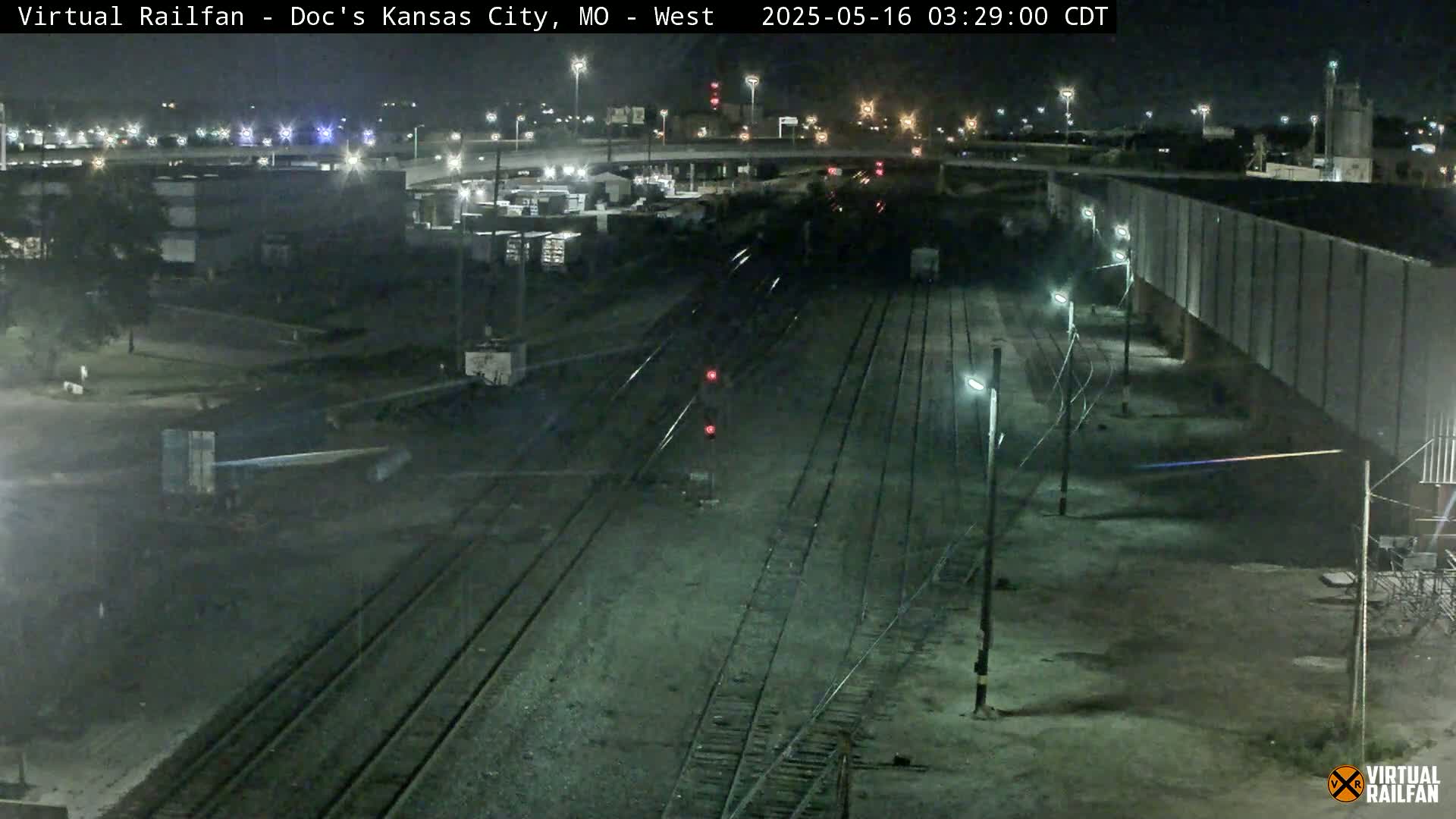 A nighttime view of railroad tracks and industrial buildings under streetlights.