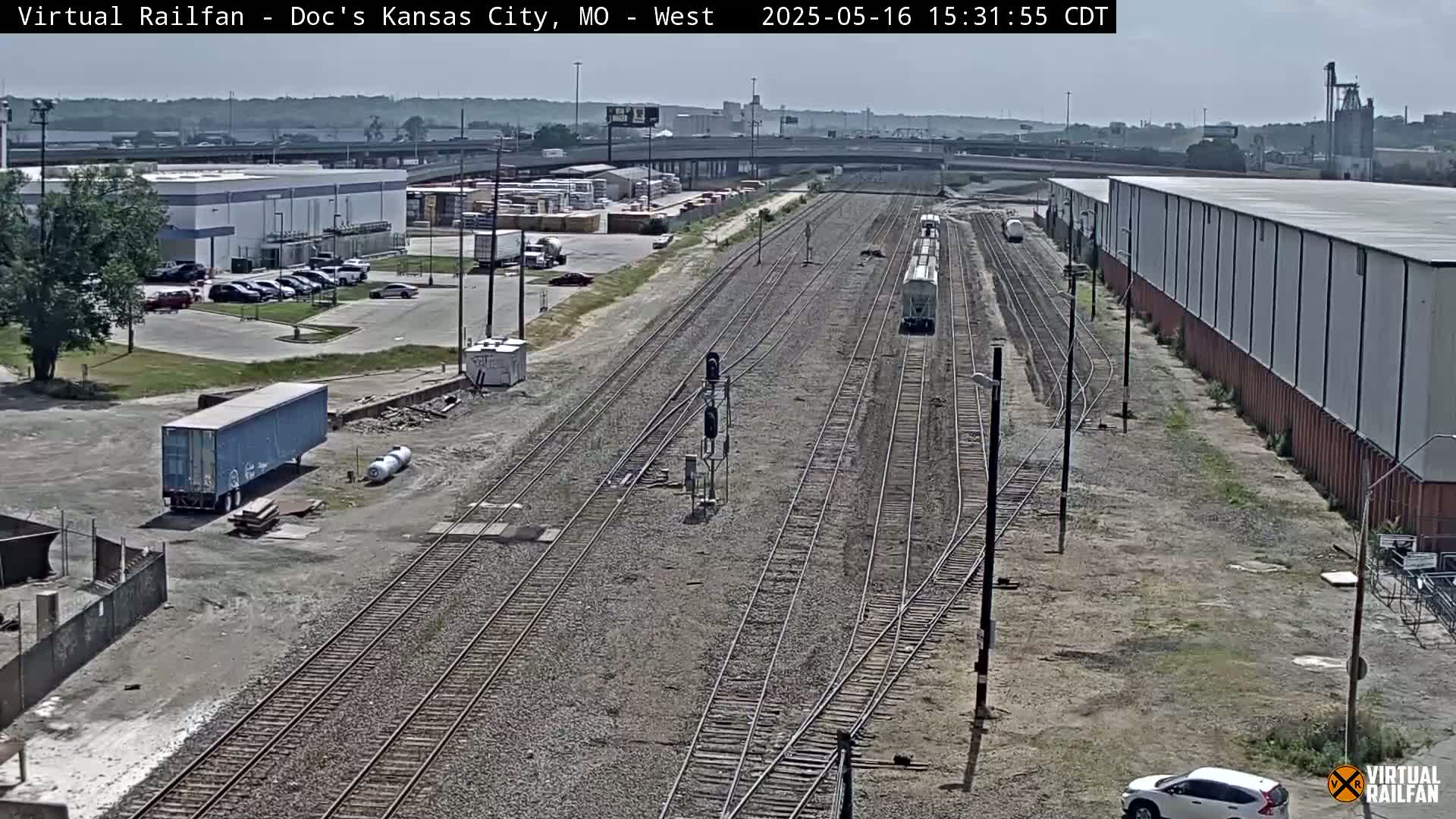 A high-angle view of a train yard with multiple train tracks, a train, and several buildings on a sunny day.