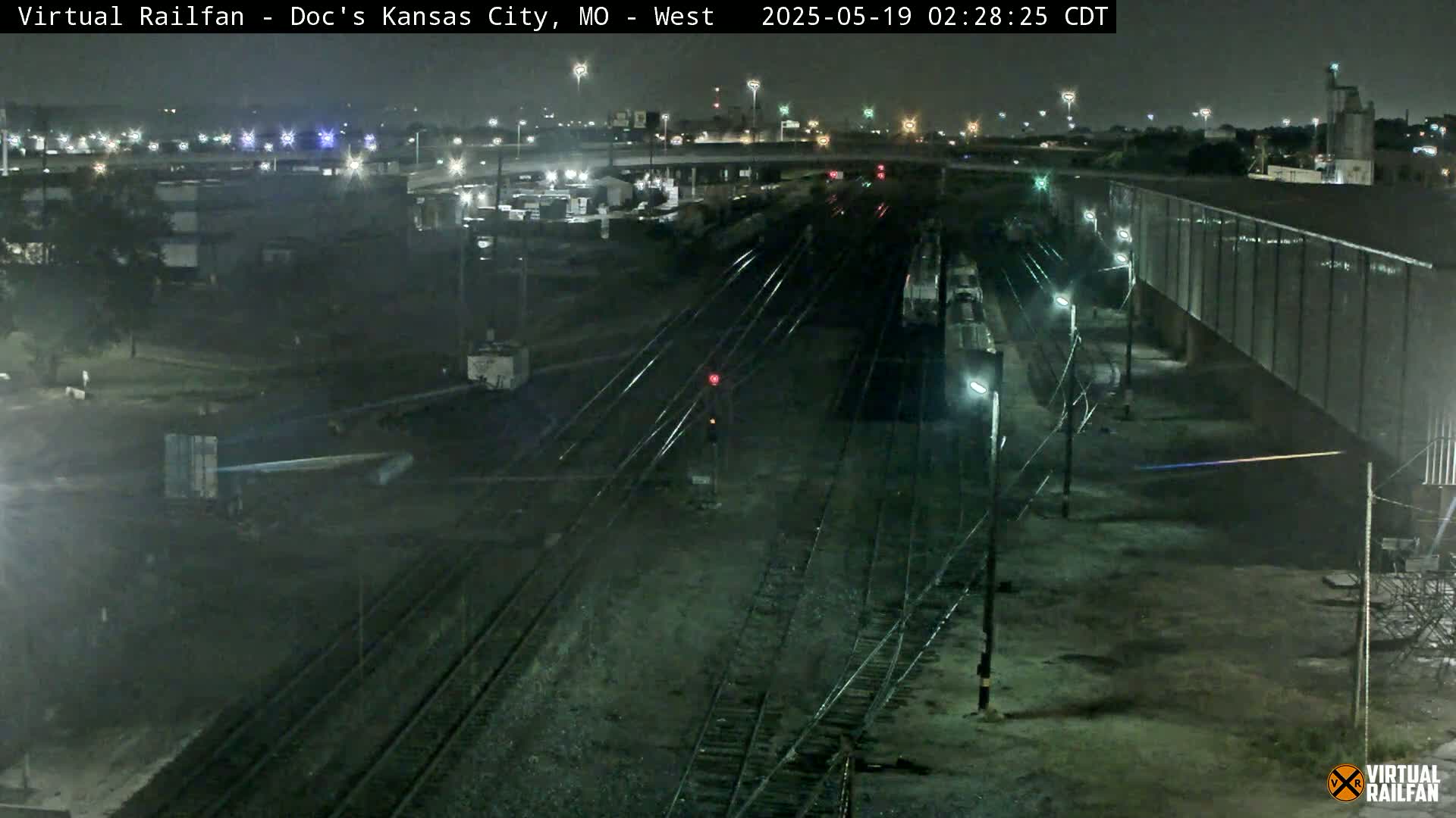 A nighttime, overhead view of a train yard with several train cars and tracks, under mostly clear skies.