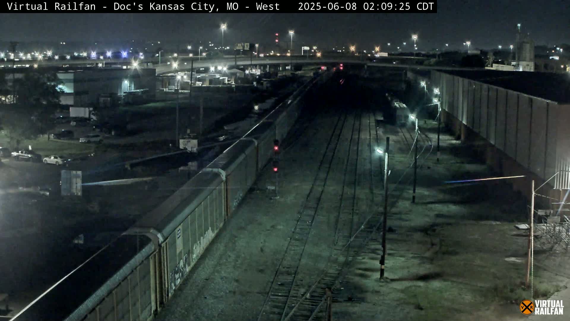 A long freight train is stopped at a railroad crossing at night, under a clear sky.