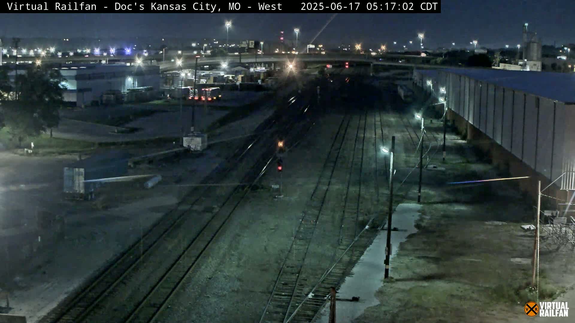 A nighttime view of railroad tracks and industrial buildings under clear skies.