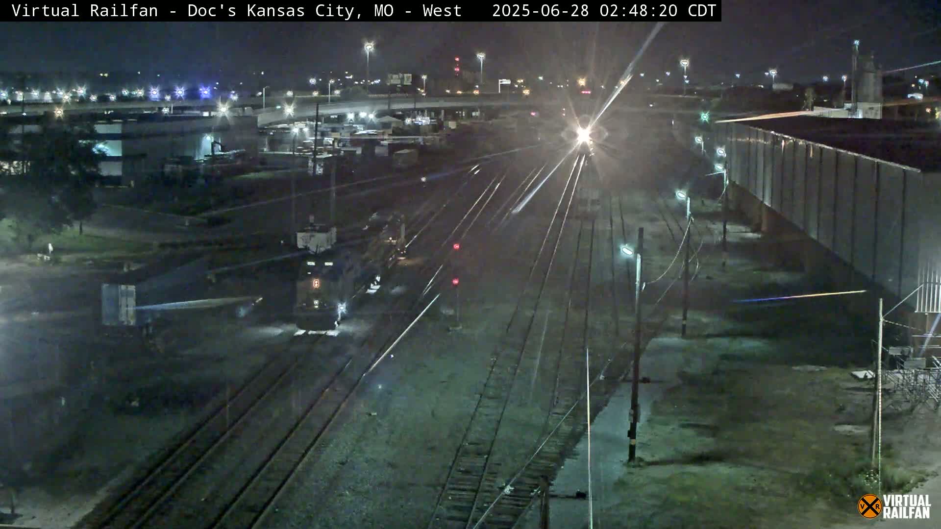 A nighttime view of a train passing through a rail yard, under clear skies.