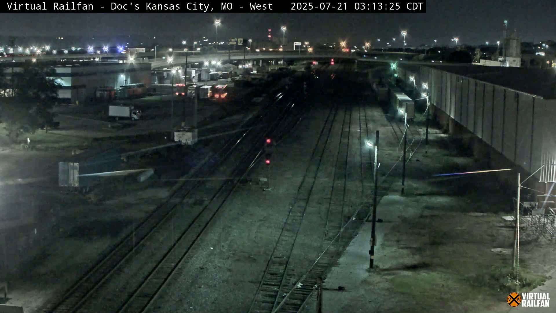 A nighttime view of railroad tracks, industrial buildings, and a roadway, under clear skies.