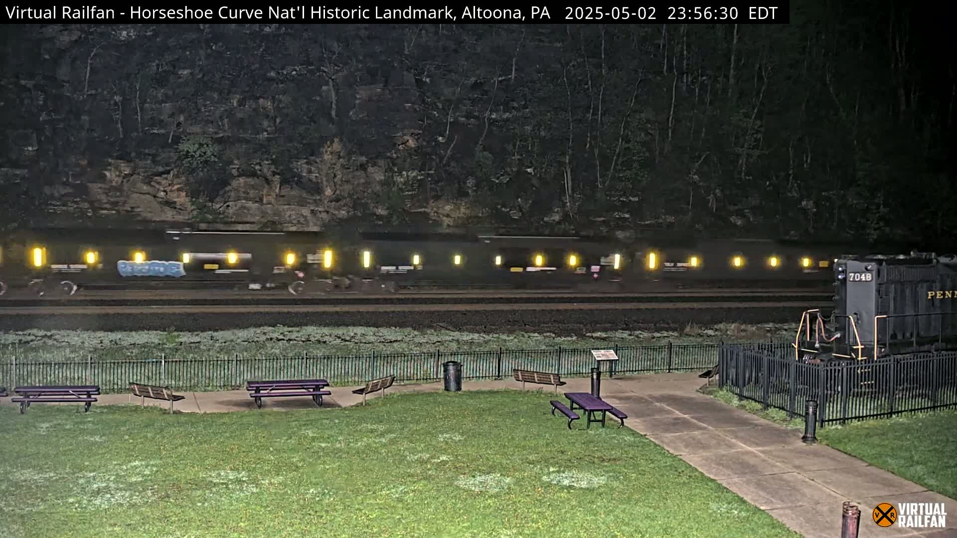 A long freight train passes by a park at night, with frost on the ground.