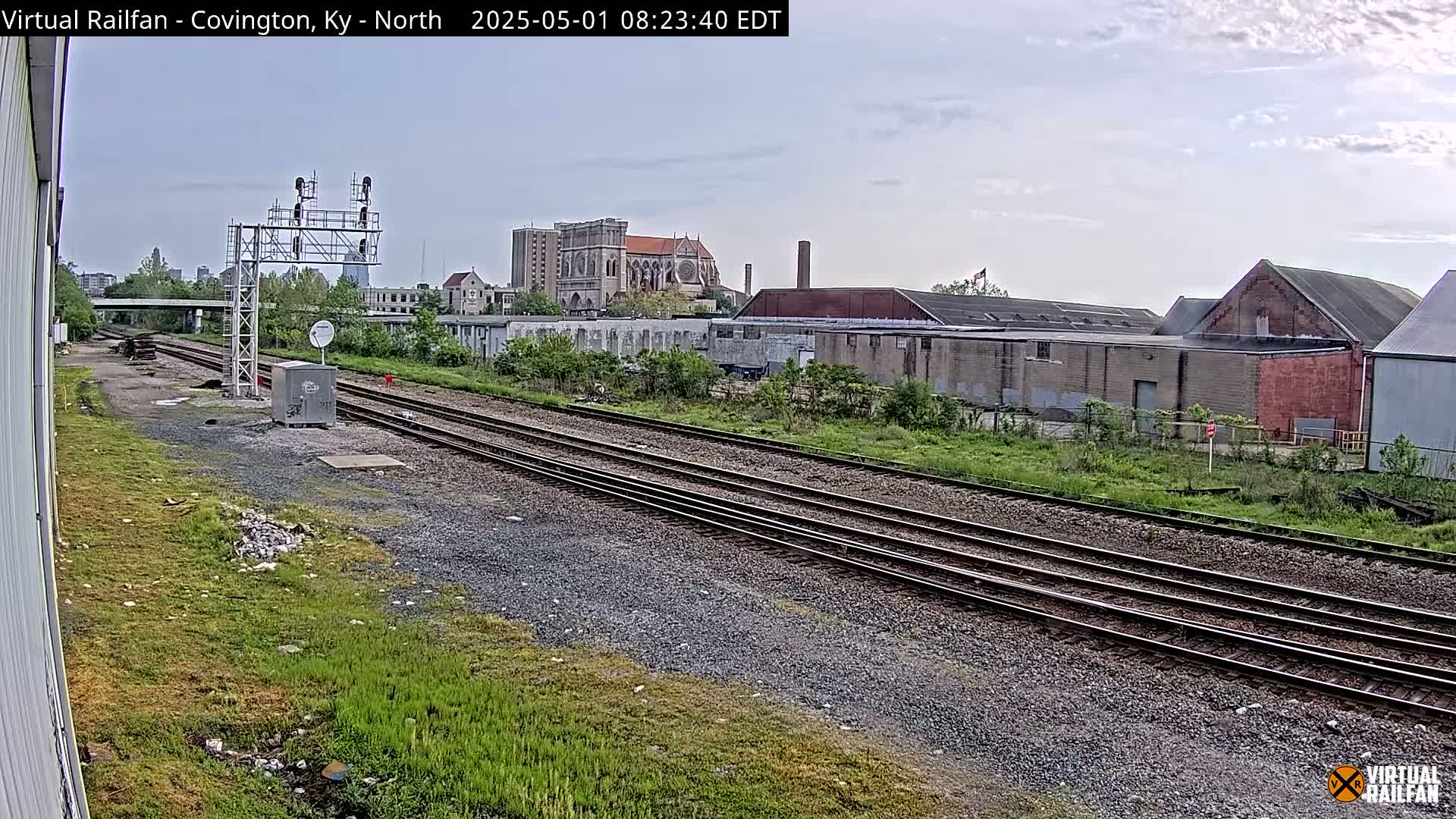 A view of railroad tracks on an overcast day, with industrial buildings and a large church visible in the background.