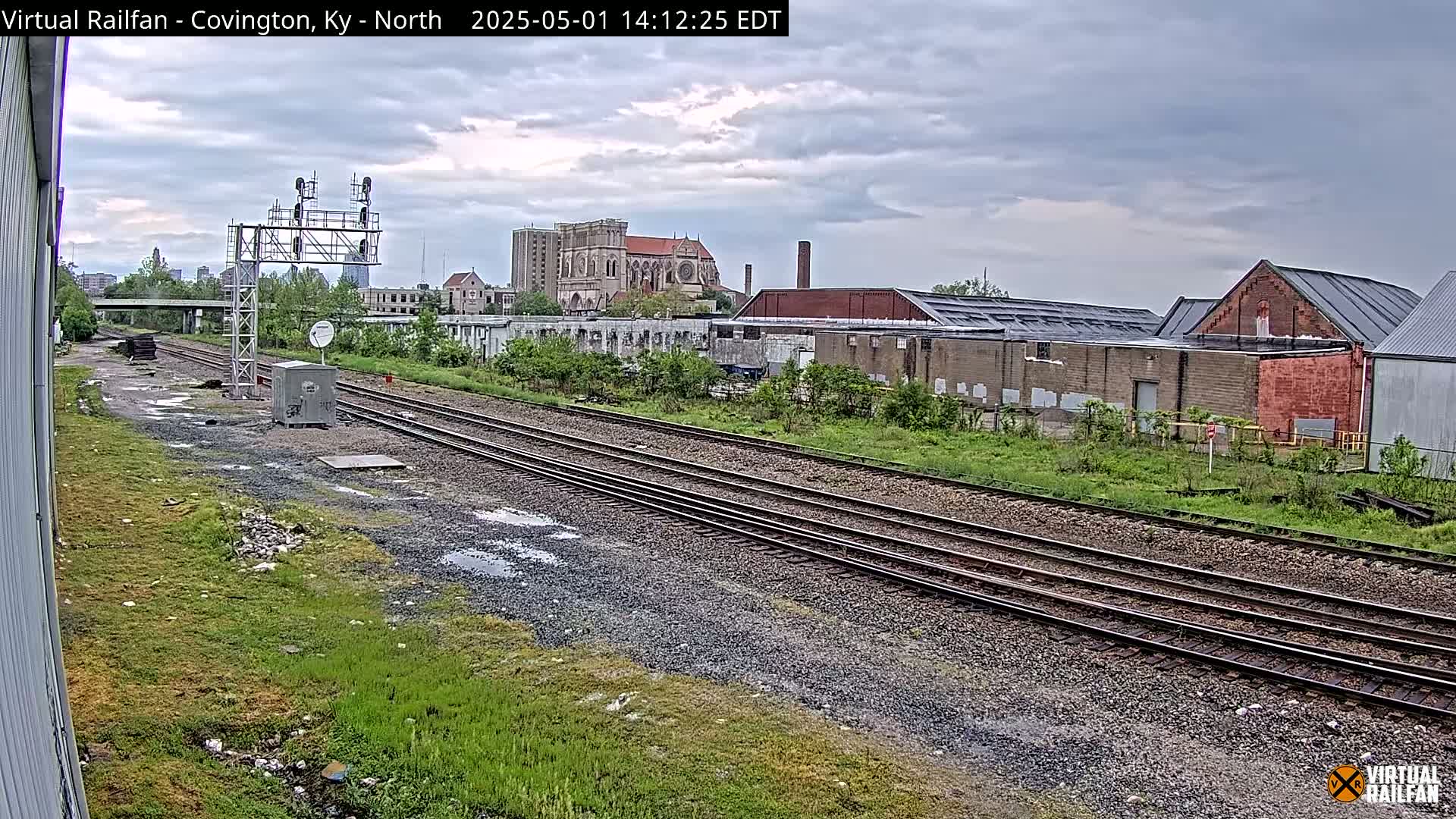 A view of railroad tracks, industrial buildings, and a large church in the background under a cloudy sky.