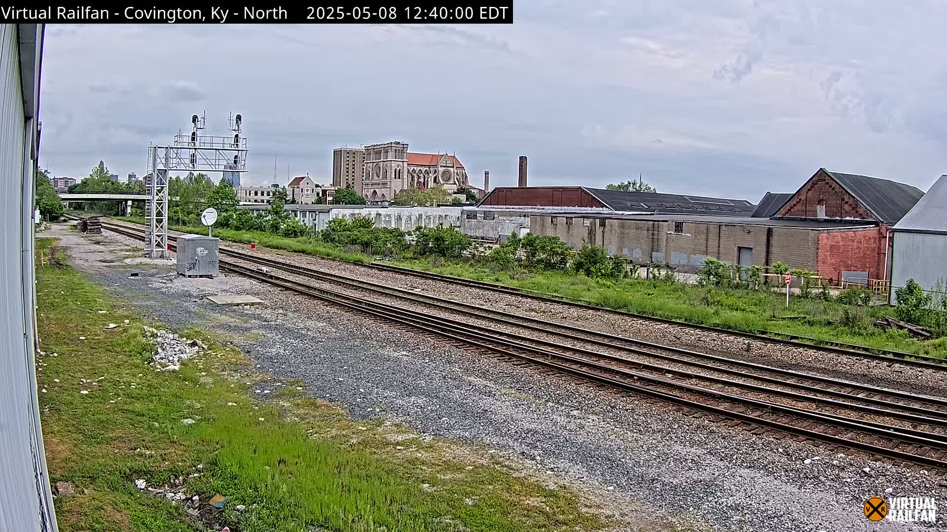 A view of several parallel train tracks, leading towards industrial buildings and a large cathedral under an overcast sky.