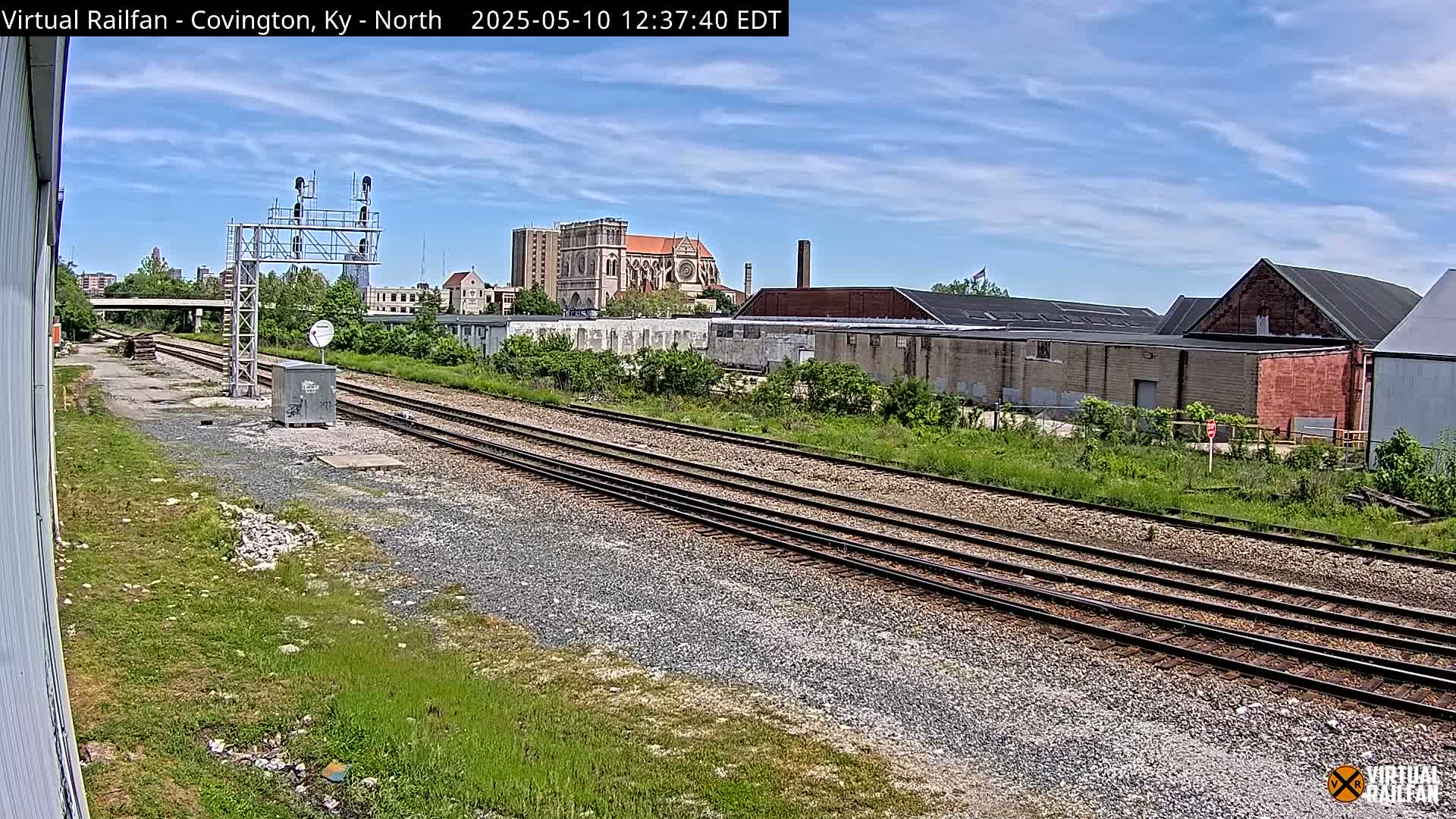 A view of railroad tracks on a sunny day, with industrial buildings and a large church visible in the distance.