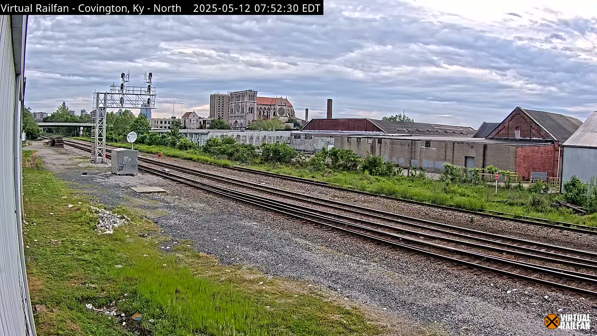A view of railroad tracks on an overcast day, with industrial buildings and a large church visible in the background.