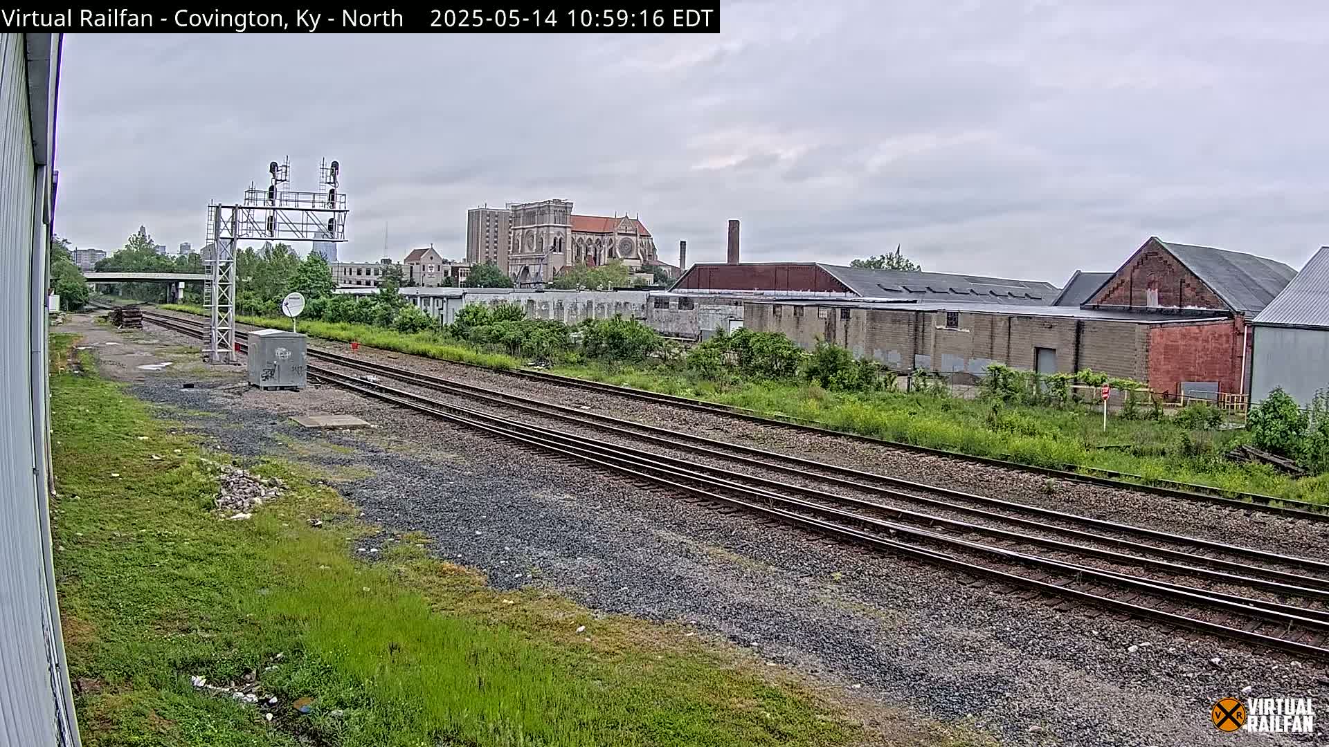A view of railroad tracks on an overcast day, with industrial buildings and a large church visible in the distance.