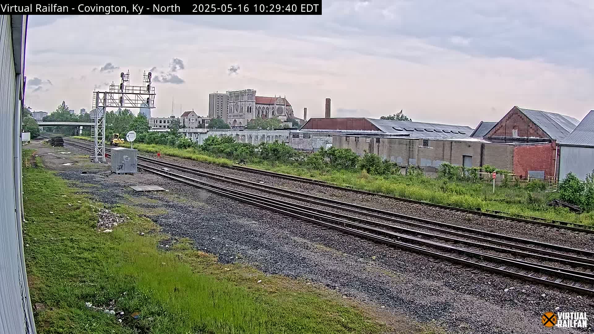 A view of railroad tracks on an overcast day, with industrial buildings and a large church visible in the background.