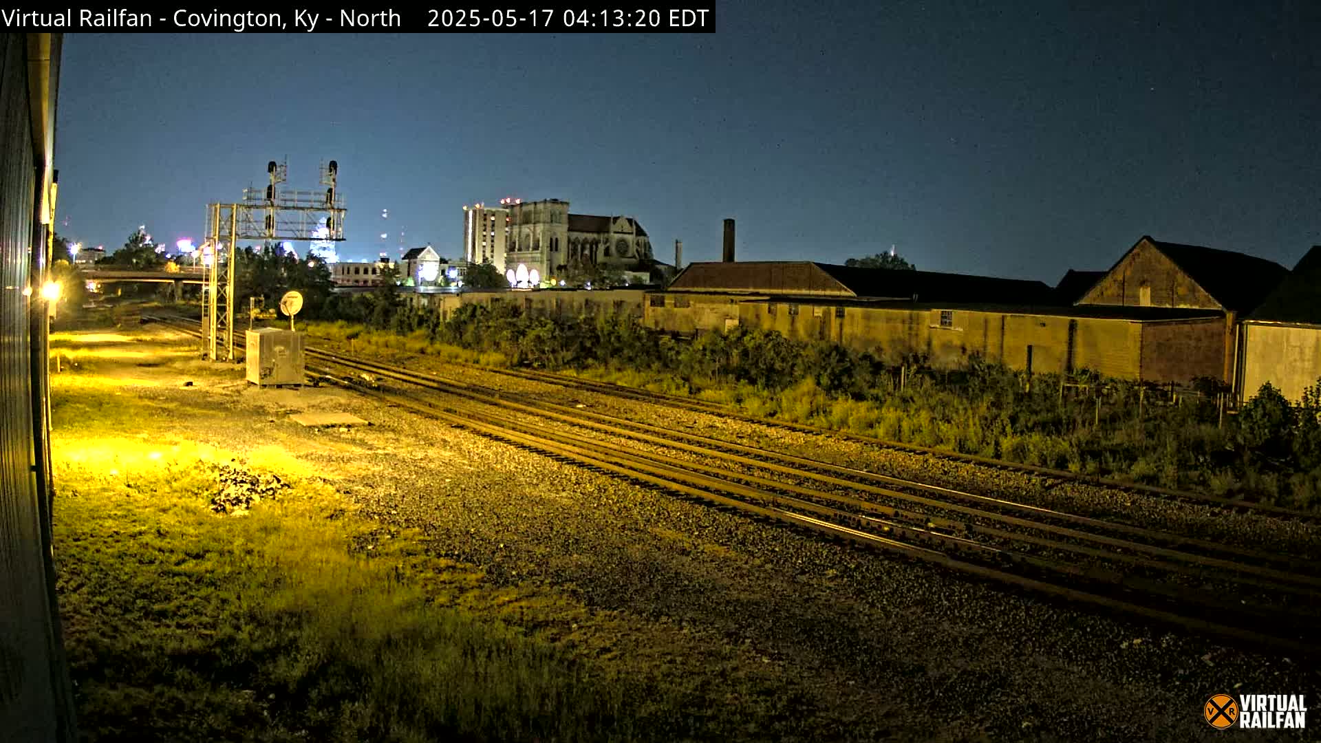 Nighttime view of multiple train tracks running alongside industrial buildings and a church under a clear, dark sky.