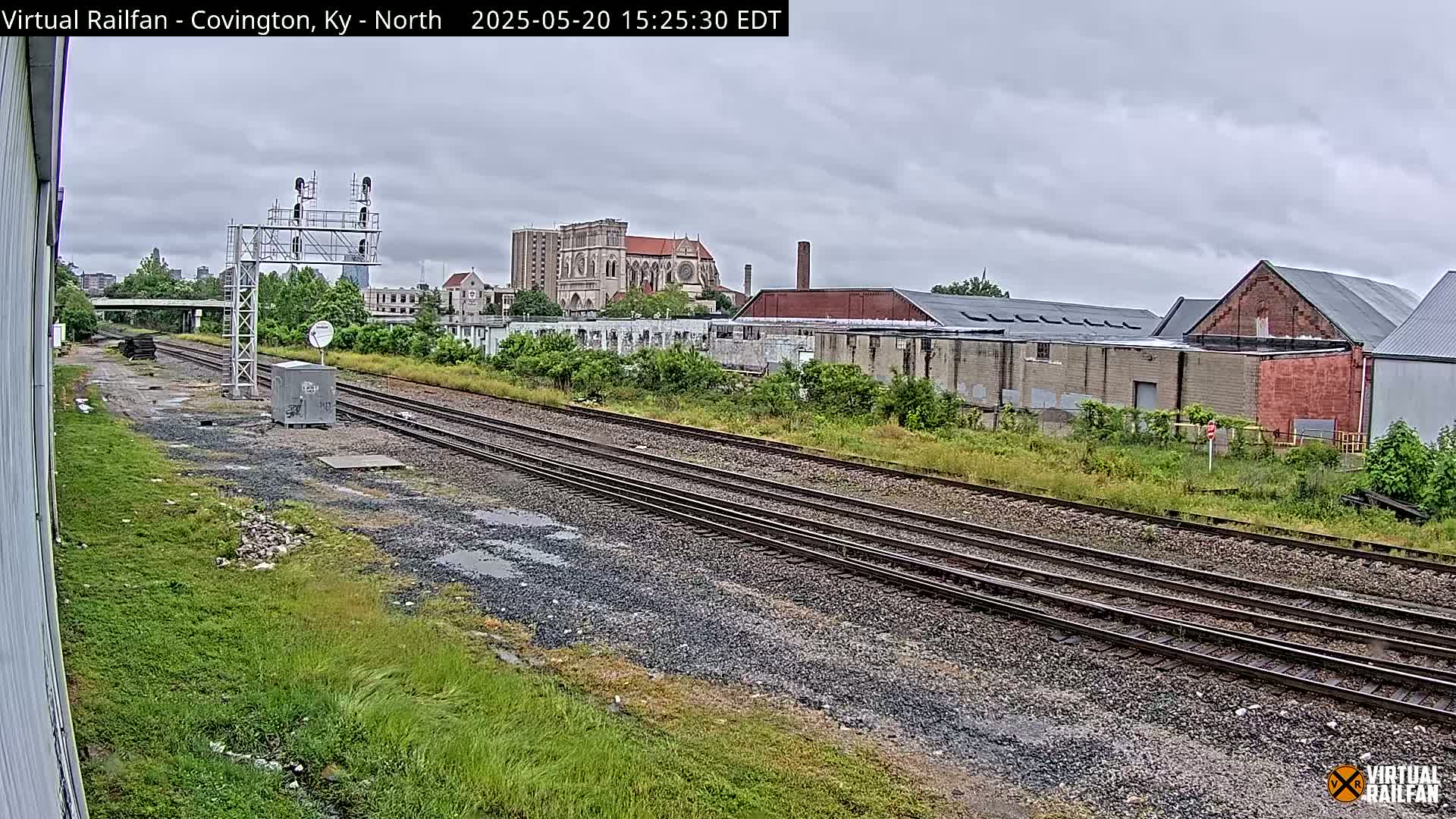 A view of railroad tracks on an overcast day, with industrial buildings and a large church visible in the distance.